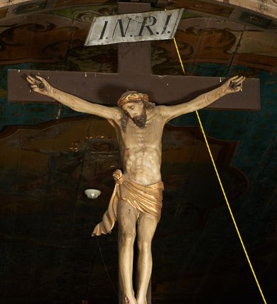 Zdjęcie nr 2: Pełnoplastyczna figura Chrystusa umarłego przybita trzema gwoździami do krzyża o prostym zakończeniu ramion. Ciało w delikatnym zwisie o horyzontalnie rozłożonych ramionach, głowa opadająca na praw bark, nogi lekko ugięte w kolanach, stopy skrzyżowane w układzie prawa na lewą. Chrystus ma pociągłą twarz, o głęboko osadzonych, zamkniętych oczach, długim, wąskim nosie i ustach o opadających kącikach, okoloną falowaną, trójkątną brodą oraz skręconymi w rurkowate pukle włosami. Na głowie ma złoconą koronę cierniową. Ciało szczupłe, wydłużone, o guzowato rzeźbionych mięśniach i żebrach klatki piersiowej oraz wygiętych stopach z podkreślonymi ścięgnami. Perizonium złocone, krótkie, ściśle przylegające do ciała, zawiązane na prawym boku, z lekko rozwianym zwisem tkaniny. Polichromia ciała naturalistyczna. 
U szczytu pionowej belki krzyża tabliczka z malowanym napisem „I.N.R.I.”, pod stopami Chrystusa przybite do krzyża wota.
