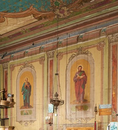 Zdjęcie nr 1: Polichromia ścian kościoła odpowiada podziałom architektonicznym wnętrza wydzielonym przez pilastry, filary i kolumny (w prezbiterium iluzjonistyczne pilastry). Malowany jasnobrązowy cokół w jednej czwartej wysokości ścian zamknięty jest profilowanym gzymsem, w jego polu znajdują się jasnozielone malowane płyciny odpowiadające szerokości podziałów wnętrza. Trzony pilastrów bladoróżowe z malowanymi czerwonymi płycinami, w prezbiterium z kapitelami korynckimi, w nawie zakończone tryglifami. Podpory podtrzymują malowane belkowanie, z jasnoróżowym fryzem i wspornikami dekorowanymi anthemionami, dźwigającymi silnie wysunięty gzyms. W nawie belkowanie malowane jest w partii środkowej (bez zaskrzynień) podtrzymywanej przez filary i kolumny. W polach pomiędzy pilastrami malowane płyciny w formie prostokątów, o szerokości przęseł, ujęte ramą dekorowaną w narożach stylizowanym akantem z kampanulami. W prezbiterium w jasnożółtych płycinach znajdują się malowane nisze w formie stojącego prostokąta zamkniętego łukiem półkolistym, ujęte profilowaną ramą, dekorowaną u góry i u dołu ornamentem roślinnym, z przedstawieniami ewangelistów i ich symboli. Na ścianie północnej znajdują się św. Mateusz, św. Marek i św. Łukasz, a na ścianie południowej, pomiędzy okami św. Jan. W nawie jasnożółte płyciny ścian wypełnione są dekoracją geometryczną w formie niebieskich i żółtych równoramiennych krzyżyków. Otwory okienne, drzwiowe i arkada kaplicy ujęte są malowanymi, imitującymi profilowanie obramieniami, dekorowanymi ornamentem roślinnym. 
Strop prezbiterium i nawy w malowanej, kolorowej, profilowanej ramie, po wewnętrznej stronie z zielono-różowym pasem zdobionym ornamentem. Pośrodku, na tle malowanej jasnoróżowej płyciny, wydzielone pole o fantazyjnym kształcie, obwiedzione pomarańczową opaską z kartuszami na każdej stronie, ujętymi ornamentem roślinnym, wypełnionymi kratką i fantazyjną dekoracją. Jasnoniebieskie pole wypełnione jest malowanymi na złoto gwiazdami. W prezbiterium, w jego centrum kolejne pole o analogicznym kształcie ze sceną Wniebowzięcia Marii, a w nawie dwa pola ze scenami Chrystusa Zmartwychwstałego i Świętej Rodziny. W partii zaskrzynień nawy malowane płyciny w zielonych opaskach i jasnoróżowych polach wypełnione ornamentem geometrycznym. Jasnozielona balustrada chóru muzycznego dekorowana malowanymi płycinami w formie prostokątów, naprzemiennie stojących i leżących, flankujących środkowy medalion, wszystkie ujęte profilowaną ramą. Pola prostokątów stojących wypełnione rozetami na jasnoczerwonym tle. Pola prostokątów leżących wypełnione przedstawieniami instrumentów i ornamentu roślinnego ukazanych na żółtym tle. W środkowym medalionie przedstawienie Dawida grającego na harfie. 















