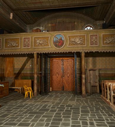 Zdjęcie nr 7: Polichromia ścian kościoła odpowiada podziałom architektonicznym wnętrza wydzielonym przez pilastry, filary i kolumny (w prezbiterium iluzjonistyczne pilastry). Malowany jasnobrązowy cokół w jednej czwartej wysokości ścian zamknięty jest profilowanym gzymsem, w jego polu znajdują się jasnozielone malowane płyciny odpowiadające szerokości podziałów wnętrza. Trzony pilastrów bladoróżowe z malowanymi czerwonymi płycinami, w prezbiterium z kapitelami korynckimi, w nawie zakończone tryglifami. Podpory podtrzymują malowane belkowanie, z jasnoróżowym fryzem i wspornikami dekorowanymi anthemionami, dźwigającymi silnie wysunięty gzyms. W nawie belkowanie malowane jest w partii środkowej (bez zaskrzynień) podtrzymywanej przez filary i kolumny. W polach pomiędzy pilastrami malowane płyciny w formie prostokątów, o szerokości przęseł, ujęte ramą dekorowaną w narożach stylizowanym akantem z kampanulami. W prezbiterium w jasnożółtych płycinach znajdują się malowane nisze w formie stojącego prostokąta zamkniętego łukiem półkolistym, ujęte profilowaną ramą, dekorowaną u góry i u dołu ornamentem roślinnym, z przedstawieniami ewangelistów i ich symboli. Na ścianie północnej znajdują się św. Mateusz, św. Marek i św. Łukasz, a na ścianie południowej, pomiędzy okami św. Jan. W nawie jasnożółte płyciny ścian wypełnione są dekoracją geometryczną w formie niebieskich i żółtych równoramiennych krzyżyków. Otwory okienne, drzwiowe i arkada kaplicy ujęte są malowanymi, imitującymi profilowanie obramieniami, dekorowanymi ornamentem roślinnym. 
Strop prezbiterium i nawy w malowanej, kolorowej, profilowanej ramie, po wewnętrznej stronie z zielono-różowym pasem zdobionym ornamentem. Pośrodku, na tle malowanej jasnoróżowej płyciny, wydzielone pole o fantazyjnym kształcie, obwiedzione pomarańczową opaską z kartuszami na każdej stronie, ujętymi ornamentem roślinnym, wypełnionymi kratką i fantazyjną dekoracją. Jasnoniebieskie pole wypełnione jest malowanymi na złoto gwiazdami. W prezbiterium, w jego centrum kolejne pole o analogicznym kształcie ze sceną Wniebowzięcia Marii, a w nawie dwa pola ze scenami Chrystusa Zmartwychwstałego i Świętej Rodziny. W partii zaskrzynień nawy malowane płyciny w zielonych opaskach i jasnoróżowych polach wypełnione ornamentem geometrycznym. Jasnozielona balustrada chóru muzycznego dekorowana malowanymi płycinami w formie prostokątów, naprzemiennie stojących i leżących, flankujących środkowy medalion, wszystkie ujęte profilowaną ramą. Pola prostokątów stojących wypełnione rozetami na jasnoczerwonym tle. Pola prostokątów leżących wypełnione przedstawieniami instrumentów i ornamentu roślinnego ukazanych na żółtym tle. W środkowym medalionie przedstawienie Dawida grającego na harfie. 















