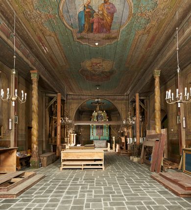 Zdjęcie nr 23: Polichromia ścian kościoła odpowiada podziałom architektonicznym wnętrza wydzielonym przez pilastry, filary i kolumny (w prezbiterium iluzjonistyczne pilastry). Malowany jasnobrązowy cokół w jednej czwartej wysokości ścian zamknięty jest profilowanym gzymsem, w jego polu znajdują się jasnozielone malowane płyciny odpowiadające szerokości podziałów wnętrza. Trzony pilastrów bladoróżowe z malowanymi czerwonymi płycinami, w prezbiterium z kapitelami korynckimi, w nawie zakończone tryglifami. Podpory podtrzymują malowane belkowanie, z jasnoróżowym fryzem i wspornikami dekorowanymi anthemionami, dźwigającymi silnie wysunięty gzyms. W nawie belkowanie malowane jest w partii środkowej (bez zaskrzynień) podtrzymywanej przez filary i kolumny. W polach pomiędzy pilastrami malowane płyciny w formie prostokątów, o szerokości przęseł, ujęte ramą dekorowaną w narożach stylizowanym akantem z kampanulami. W prezbiterium w jasnożółtych płycinach znajdują się malowane nisze w formie stojącego prostokąta zamkniętego łukiem półkolistym, ujęte profilowaną ramą, dekorowaną u góry i u dołu ornamentem roślinnym, z przedstawieniami ewangelistów i ich symboli. Na ścianie północnej znajdują się św. Mateusz, św. Marek i św. Łukasz, a na ścianie południowej, pomiędzy okami św. Jan. W nawie jasnożółte płyciny ścian wypełnione są dekoracją geometryczną w formie niebieskich i żółtych równoramiennych krzyżyków. Otwory okienne, drzwiowe i arkada kaplicy ujęte są malowanymi, imitującymi profilowanie obramieniami, dekorowanymi ornamentem roślinnym. 
Strop prezbiterium i nawy w malowanej, kolorowej, profilowanej ramie, po wewnętrznej stronie z zielono-różowym pasem zdobionym ornamentem. Pośrodku, na tle malowanej jasnoróżowej płyciny, wydzielone pole o fantazyjnym kształcie, obwiedzione pomarańczową opaską z kartuszami na każdej stronie, ujętymi ornamentem roślinnym, wypełnionymi kratką i fantazyjną dekoracją. Jasnoniebieskie pole wypełnione jest malowanymi na złoto gwiazdami. W prezbiterium, w jego centrum kolejne pole o analogicznym kształcie ze sceną Wniebowzięcia Marii, a w nawie dwa pola ze scenami Chrystusa Zmartwychwstałego i Świętej Rodziny. W partii zaskrzynień nawy malowane płyciny w zielonych opaskach i jasnoróżowych polach wypełnione ornamentem geometrycznym. Jasnozielona balustrada chóru muzycznego dekorowana malowanymi płycinami w formie prostokątów, naprzemiennie stojących i leżących, flankujących środkowy medalion, wszystkie ujęte profilowaną ramą. Pola prostokątów stojących wypełnione rozetami na jasnoczerwonym tle. Pola prostokątów leżących wypełnione przedstawieniami instrumentów i ornamentu roślinnego ukazanych na żółtym tle. W środkowym medalionie przedstawienie Dawida grającego na harfie. 















