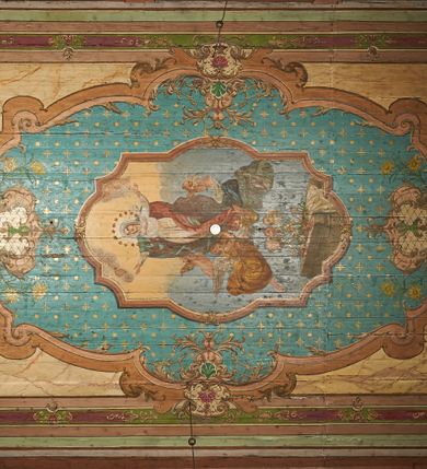 Zdjęcie nr 4: Polichromia ścian kościoła odpowiada podziałom architektonicznym wnętrza wydzielonym przez pilastry, filary i kolumny (w prezbiterium iluzjonistyczne pilastry). Malowany jasnobrązowy cokół w jednej czwartej wysokości ścian zamknięty jest profilowanym gzymsem, w jego polu znajdują się jasnozielone malowane płyciny odpowiadające szerokości podziałów wnętrza. Trzony pilastrów bladoróżowe z malowanymi czerwonymi płycinami, w prezbiterium z kapitelami korynckimi, w nawie zakończone tryglifami. Podpory podtrzymują malowane belkowanie, z jasnoróżowym fryzem i wspornikami dekorowanymi anthemionami, dźwigającymi silnie wysunięty gzyms. W nawie belkowanie malowane jest w partii środkowej (bez zaskrzynień) podtrzymywanej przez filary i kolumny. W polach pomiędzy pilastrami malowane płyciny w formie prostokątów, o szerokości przęseł, ujęte ramą dekorowaną w narożach stylizowanym akantem z kampanulami. W prezbiterium w jasnożółtych płycinach znajdują się malowane nisze w formie stojącego prostokąta zamkniętego łukiem półkolistym, ujęte profilowaną ramą, dekorowaną u góry i u dołu ornamentem roślinnym, z przedstawieniami ewangelistów i ich symboli. Na ścianie północnej znajdują się św. Mateusz, św. Marek i św. Łukasz, a na ścianie południowej, pomiędzy okami św. Jan. W nawie jasnożółte płyciny ścian wypełnione są dekoracją geometryczną w formie niebieskich i żółtych równoramiennych krzyżyków. Otwory okienne, drzwiowe i arkada kaplicy ujęte są malowanymi, imitującymi profilowanie obramieniami, dekorowanymi ornamentem roślinnym. 
Strop prezbiterium i nawy w malowanej, kolorowej, profilowanej ramie, po wewnętrznej stronie z zielono-różowym pasem zdobionym ornamentem. Pośrodku, na tle malowanej jasnoróżowej płyciny, wydzielone pole o fantazyjnym kształcie, obwiedzione pomarańczową opaską z kartuszami na każdej stronie, ujętymi ornamentem roślinnym, wypełnionymi kratką i fantazyjną dekoracją. Jasnoniebieskie pole wypełnione jest malowanymi na złoto gwiazdami. W prezbiterium, w jego centrum kolejne pole o analogicznym kształcie ze sceną Wniebowzięcia Marii, a w nawie dwa pola ze scenami Chrystusa Zmartwychwstałego i Świętej Rodziny. W partii zaskrzynień nawy malowane płyciny w zielonych opaskach i jasnoróżowych polach wypełnione ornamentem geometrycznym. Jasnozielona balustrada chóru muzycznego dekorowana malowanymi płycinami w formie prostokątów, naprzemiennie stojących i leżących, flankujących środkowy medalion, wszystkie ujęte profilowaną ramą. Pola prostokątów stojących wypełnione rozetami na jasnoczerwonym tle. Pola prostokątów leżących wypełnione przedstawieniami instrumentów i ornamentu roślinnego ukazanych na żółtym tle. W środkowym medalionie przedstawienie Dawida grającego na harfie. 















