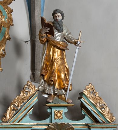 Zdjęcie nr 2: Rzeźba przedstawiająca św. Pawła ścięta z tyłu, drążona, ustawiona na rzeźbionym fragmencie skały. Figura ukazana frontalnie, w prawej wyciągniętej ręce trzyma otwartą księgę, a w lewej miecz, skierowany ostrzem w dół. Twarz szeroka, usta otwarte, niskie czoło, okolona długą i bujną brodą, układającą się w dwa pukle, opadające na pierś. Włosy średniej długości, zasłaniające uszy, zawinięte do tyłu w szerokie pukle. Święty ubrany jest w srebrzoną, długą suknię, rozwianą u spodu oraz złocony płaszcz przerzucony przez prawe ramie, drapowany w grube fałdy; na stopach ma założone sandały. Polichromia naturalistyczna w odsłoniętych partiach ciała, szaty i atrybuty złocone oraz srebrzone.