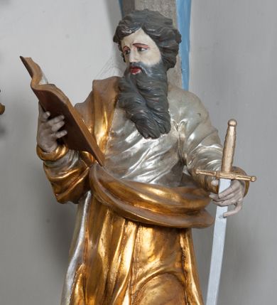 Zdjęcie nr 1: Rzeźba przedstawiająca św. Pawła ścięta z tyłu, drążona, ustawiona na rzeźbionym fragmencie skały. Figura ukazana frontalnie, w prawej wyciągniętej ręce trzyma otwartą księgę, a w lewej miecz, skierowany ostrzem w dół. Twarz szeroka, usta otwarte, niskie czoło, okolona długą i bujną brodą, układającą się w dwa pukle, opadające na pierś. Włosy średniej długości, zasłaniające uszy, zawinięte do tyłu w szerokie pukle. Święty ubrany jest w srebrzoną, długą suknię, rozwianą u spodu oraz złocony płaszcz przerzucony przez prawe ramie, drapowany w grube fałdy; na stopach ma założone sandały. Polichromia naturalistyczna w odsłoniętych partiach ciała, szaty i atrybuty złocone oraz srebrzone.
