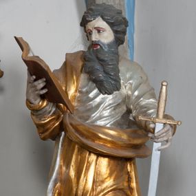 Zdjęcie nr 1: Rzeźba przedstawiająca św. Pawła ścięta z tyłu, drążona, ustawiona na rzeźbionym fragmencie skały. Figura ukazana frontalnie, w prawej wyciągniętej ręce trzyma otwartą księgę, a w lewej miecz, skierowany ostrzem w dół. Twarz szeroka, usta otwarte, niskie czoło, okolona długą i bujną brodą, układającą się w dwa pukle, opadające na pierś. Włosy średniej długości, zasłaniające uszy, zawinięte do tyłu w szerokie pukle. Święty ubrany jest w srebrzoną, długą suknię, rozwianą u spodu oraz złocony płaszcz przerzucony przez prawe ramie, drapowany w grube fałdy; na stopach ma założone sandały. Polichromia naturalistyczna w odsłoniętych partiach ciała, szaty i atrybuty złocone oraz srebrzone.