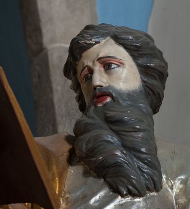 Zdjęcie nr 5: Rzeźba przedstawiająca św. Pawła ścięta z tyłu, drążona, ustawiona na rzeźbionym fragmencie skały. Figura ukazana frontalnie, w prawej wyciągniętej ręce trzyma otwartą księgę, a w lewej miecz, skierowany ostrzem w dół. Twarz szeroka, usta otwarte, niskie czoło, okolona długą i bujną brodą, układającą się w dwa pukle, opadające na pierś. Włosy średniej długości, zasłaniające uszy, zawinięte do tyłu w szerokie pukle. Święty ubrany jest w srebrzoną, długą suknię, rozwianą u spodu oraz złocony płaszcz przerzucony przez prawe ramie, drapowany w grube fałdy; na stopach ma założone sandały. Polichromia naturalistyczna w odsłoniętych partiach ciała, szaty i atrybuty złocone oraz srebrzone.