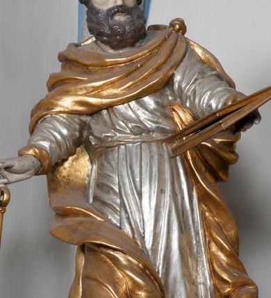 Zdjęcie nr 5: Rzeźba przedstawiająca św. Piotra, ścięta z tyłu, drążona, ustawiona na rzeźbionym fragmencie skały. Figura ukazana frontalnie z głową skierowaną delikatnie w prawo, obie ręce rozłożone w boki: w lewej trzyma zamkniętą księgę, a w prawej klucze. Twarz szeroka z otwartymi ustami, okolona gęstą brodą, włosy w postaci pukli po bokach i na czubku głowy. Święty ubrany jest w delikatnie drapowaną suknię, przepasaną w talii oraz płaszcz zapięty na lewym ramieniu, opadający na plecy i na prawe kolano, drapowany w grube fałdy, zawijające się przy brzegach; na stopach ma sandały. Polichromia naturalistyczna w odsłoniętych partiach ciała, szaty i atrybuty złocone oraz srebrzone.