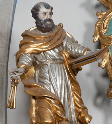 Zdjęcie nr 1: Rzeźba przedstawiająca św. Piotra, ścięta z tyłu, drążona, ustawiona na rzeźbionym fragmencie skały. Figura ukazana frontalnie z głową skierowaną delikatnie w prawo, obie ręce rozłożone w boki: w lewej trzyma zamkniętą księgę, a w prawej klucze. Twarz szeroka z otwartymi ustami, okolona gęstą brodą, włosy w postaci pukli po bokach i na czubku głowy. Święty ubrany jest w delikatnie drapowaną suknię, przepasaną w talii oraz płaszcz zapięty na lewym ramieniu, opadający na plecy i na prawe kolano, drapowany w grube fałdy, zawijające się przy brzegach; na stopach ma sandały. Polichromia naturalistyczna w odsłoniętych partiach ciała, szaty i atrybuty złocone oraz srebrzone.