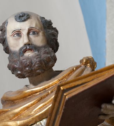 Zdjęcie nr 6: Rzeźba przedstawiająca św. Piotra, ścięta z tyłu, drążona, ustawiona na rzeźbionym fragmencie skały. Figura ukazana frontalnie z głową skierowaną delikatnie w prawo, obie ręce rozłożone w boki: w lewej trzyma zamkniętą księgę, a w prawej klucze. Twarz szeroka z otwartymi ustami, okolona gęstą brodą, włosy w postaci pukli po bokach i na czubku głowy. Święty ubrany jest w delikatnie drapowaną suknię, przepasaną w talii oraz płaszcz zapięty na lewym ramieniu, opadający na plecy i na prawe kolano, drapowany w grube fałdy, zawijające się przy brzegach; na stopach ma sandały. Polichromia naturalistyczna w odsłoniętych partiach ciała, szaty i atrybuty złocone oraz srebrzone.