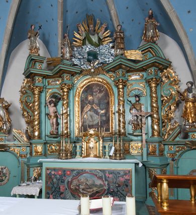 Zdjęcie nr 35: Nastawa ołtarzowa architektoniczna, jednokondygnacyjna, trójosiowa ze zwieńczeniem i z bramkami. Ołtarz prostopadłościenny, drewniany, mensa drewniana z kamiennym portatylem. Antependium w formie leżącego prostokąta ujętego złoconą, profilowaną ramą. W polu obraz malowany olejem na płótnie. W centrum kartusz w kształcie wydłużonego czwórliścia, dekorowany muszlą i wolutami z przedstawieniem pejzażu i widokiem na Golgotę. Po bokach kartusza bujne gałązki kwiatów. Tabernakulum w formie prostopadłościennej skrzynki o wypukłej ścianie frontowej, na profilowanym cokole, zamknięte profilowanym gzymsem, ujęte uszami utworzonymi z liści. Nad drzwiczkami, na gzymsie kartusz z niewielkim krucyfiksem. Powyżej tron wystawienia w formie profilowanej podstawy dekorowanej liśćmi. Na ściance frontowej tabernakulum profilowana rama w kształcie stojącego prostokąta zamkniętego łukiem nadwieszonym, w polu drzwiczki w formie stojącego prostokąta z przedstawieniem kielicha w glorii, powyżej drzwiczek winne grono. 

Nastawa ustawiona na zdwojonym cokole, dekorowanym wijącym się akantem. Osie kondygnacji wydzielone dwiema parami pilastrów oraz ustawionymi ukośnie kolumnami. Podpory dźwigają pełne belkowanie, przerwane nad polem środkowym i wyłamane nad osiami bocznymi, na których skraju ustawiony jest ukośnie przerwany, wolutowy przyczółek. Kolumny o kręconych trzonach, owinięte wicią liści akantu, kapitele korynckie; imposty ustawione pod kątem. W polu środkowym rama w kształcie stojącego prostokąta zamkniętego łukiem półkolistym z obrazem św. Kwiryna. W osiach bocznych płytkie płyciny, zwieńczone konchą z figurami św. Sebastiana po lewej stronie i św. Jana Nepomucena po prawej stronie, ustawionymi na wspornikach. Kondygnacja ujęta jest po bokach szerokimi uszami utworzonymi z liści akantu i karbowanej wstęgi. Fryz nad osiami bocznymi zdobiony kartuszami, we fryzie impostów z dwóch stron rozety; przyłucza osi bocznych dekorowane akantem.

W zwieńczeniu rzeźbiona półpostać Boga Ojca na obłoku z widocznym poniżej fragmentem globu ziemskiego i gołębicą Ducha Świętego; całość ukazana na tle promienistej glorii. Na belkowaniu, na osiach podpór wewnętrznych ustawione są rzeźby: św. Rocha  po lewej stronie i św. Wawrzyńca po prawej, a na zewnętrznych osiach retabulum rzeźby: Karola Boromeusza po lewej stronie i św. Stefana po prawej.

Nastawa ołtarzowa ujęta jest po bokach szerokimi bramkami w kształcie stojących prostokątów z drzwiczkami zamkniętymi półkoliście. Bramki ujęte są pilastrami o kanelowanych trzonach i fantazyjnych kapitelach, wspierających niepełne belkowanie oraz przerwany przyczółek. Nad bramkami ustawione są na cokołach rzeźby: św. Piotra po lewej stronie i św. Pawła po prawej. W polu drzwiczek owalne kartusze z herbem Görgey. W prawym kartuszu opisanym słowami: „BALTHAZAR GÖRGEI SENIOR”. Nad arkadami bramek są muszle, w przyłuczach akant, we fryzie rozety, a przerwany przyczółek dekorowany jest akantem. Struktura w całości polichromowana w odcieniu bladozielonym; ornamentyka, kolumny i profilowania złocone, detale srebrzone.