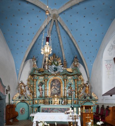 Zdjęcie nr 2: Nastawa ołtarzowa architektoniczna, jednokondygnacyjna, trójosiowa ze zwieńczeniem i z bramkami. Ołtarz prostopadłościenny, drewniany, mensa drewniana z kamiennym portatylem. Antependium w formie leżącego prostokąta ujętego złoconą, profilowaną ramą. W polu obraz malowany olejem na płótnie. W centrum kartusz w kształcie wydłużonego czwórliścia, dekorowany muszlą i wolutami z przedstawieniem pejzażu i widokiem na Golgotę. Po bokach kartusza bujne gałązki kwiatów. Tabernakulum w formie prostopadłościennej skrzynki o wypukłej ścianie frontowej, na profilowanym cokole, zamknięte profilowanym gzymsem, ujęte uszami utworzonymi z liści. Nad drzwiczkami, na gzymsie kartusz z niewielkim krucyfiksem. Powyżej tron wystawienia w formie profilowanej podstawy dekorowanej liśćmi. Na ściance frontowej tabernakulum profilowana rama w kształcie stojącego prostokąta zamkniętego łukiem nadwieszonym, w polu drzwiczki w formie stojącego prostokąta z przedstawieniem kielicha w glorii, powyżej drzwiczek winne grono. 

Nastawa ustawiona na zdwojonym cokole, dekorowanym wijącym się akantem. Osie kondygnacji wydzielone dwiema parami pilastrów oraz ustawionymi ukośnie kolumnami. Podpory dźwigają pełne belkowanie, przerwane nad polem środkowym i wyłamane nad osiami bocznymi, na których skraju ustawiony jest ukośnie przerwany, wolutowy przyczółek. Kolumny o kręconych trzonach, owinięte wicią liści akantu, kapitele korynckie; imposty ustawione pod kątem. W polu środkowym rama w kształcie stojącego prostokąta zamkniętego łukiem półkolistym z obrazem św. Kwiryna. W osiach bocznych płytkie płyciny, zwieńczone konchą z figurami św. Sebastiana po lewej stronie i św. Jana Nepomucena po prawej stronie, ustawionymi na wspornikach. Kondygnacja ujęta jest po bokach szerokimi uszami utworzonymi z liści akantu i karbowanej wstęgi. Fryz nad osiami bocznymi zdobiony kartuszami, we fryzie impostów z dwóch stron rozety; przyłucza osi bocznych dekorowane akantem.

W zwieńczeniu rzeźbiona półpostać Boga Ojca na obłoku z widocznym poniżej fragmentem globu ziemskiego i gołębicą Ducha Świętego; całość ukazana na tle promienistej glorii. Na belkowaniu, na osiach podpór wewnętrznych ustawione są rzeźby: św. Rocha  po lewej stronie i św. Wawrzyńca po prawej, a na zewnętrznych osiach retabulum rzeźby: Karola Boromeusza po lewej stronie i św. Stefana po prawej.

Nastawa ołtarzowa ujęta jest po bokach szerokimi bramkami w kształcie stojących prostokątów z drzwiczkami zamkniętymi półkoliście. Bramki ujęte są pilastrami o kanelowanych trzonach i fantazyjnych kapitelach, wspierających niepełne belkowanie oraz przerwany przyczółek. Nad bramkami ustawione są na cokołach rzeźby: św. Piotra po lewej stronie i św. Pawła po prawej. W polu drzwiczek owalne kartusze z herbem Görgey. W prawym kartuszu opisanym słowami: „BALTHAZAR GÖRGEI SENIOR”. Nad arkadami bramek są muszle, w przyłuczach akant, we fryzie rozety, a przerwany przyczółek dekorowany jest akantem. Struktura w całości polichromowana w odcieniu bladozielonym; ornamentyka, kolumny i profilowania złocone, detale srebrzone.