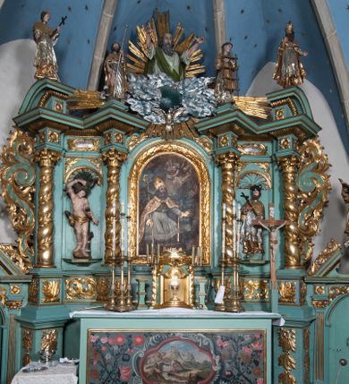 Zdjęcie nr 1: Nastawa ołtarzowa architektoniczna, jednokondygnacyjna, trójosiowa ze zwieńczeniem i z bramkami. Ołtarz prostopadłościenny, drewniany, mensa drewniana z kamiennym portatylem. Antependium w formie leżącego prostokąta ujętego złoconą, profilowaną ramą. W polu obraz malowany olejem na płótnie. W centrum kartusz w kształcie wydłużonego czwórliścia, dekorowany muszlą i wolutami z przedstawieniem pejzażu i widokiem na Golgotę. Po bokach kartusza bujne gałązki kwiatów. Tabernakulum w formie prostopadłościennej skrzynki o wypukłej ścianie frontowej, na profilowanym cokole, zamknięte profilowanym gzymsem, ujęte uszami utworzonymi z liści. Nad drzwiczkami, na gzymsie kartusz z niewielkim krucyfiksem. Powyżej tron wystawienia w formie profilowanej podstawy dekorowanej liśćmi. Na ściance frontowej tabernakulum profilowana rama w kształcie stojącego prostokąta zamkniętego łukiem nadwieszonym, w polu drzwiczki w formie stojącego prostokąta z przedstawieniem kielicha w glorii, powyżej drzwiczek winne grono. 

Nastawa ustawiona na zdwojonym cokole, dekorowanym wijącym się akantem. Osie kondygnacji wydzielone dwiema parami pilastrów oraz ustawionymi ukośnie kolumnami. Podpory dźwigają pełne belkowanie, przerwane nad polem środkowym i wyłamane nad osiami bocznymi, na których skraju ustawiony jest ukośnie przerwany, wolutowy przyczółek. Kolumny o kręconych trzonach, owinięte wicią liści akantu, kapitele korynckie; imposty ustawione pod kątem. W polu środkowym rama w kształcie stojącego prostokąta zamkniętego łukiem półkolistym z obrazem św. Kwiryna. W osiach bocznych płytkie płyciny, zwieńczone konchą z figurami św. Sebastiana po lewej stronie i św. Jana Nepomucena po prawej stronie, ustawionymi na wspornikach. Kondygnacja ujęta jest po bokach szerokimi uszami utworzonymi z liści akantu i karbowanej wstęgi. Fryz nad osiami bocznymi zdobiony kartuszami, we fryzie impostów z dwóch stron rozety; przyłucza osi bocznych dekorowane akantem.

W zwieńczeniu rzeźbiona półpostać Boga Ojca na obłoku z widocznym poniżej fragmentem globu ziemskiego i gołębicą Ducha Świętego; całość ukazana na tle promienistej glorii. Na belkowaniu, na osiach podpór wewnętrznych ustawione są rzeźby: św. Rocha  po lewej stronie i św. Wawrzyńca po prawej, a na zewnętrznych osiach retabulum rzeźby: Karola Boromeusza po lewej stronie i św. Stefana po prawej.

Nastawa ołtarzowa ujęta jest po bokach szerokimi bramkami w kształcie stojących prostokątów z drzwiczkami zamkniętymi półkoliście. Bramki ujęte są pilastrami o kanelowanych trzonach i fantazyjnych kapitelach, wspierających niepełne belkowanie oraz przerwany przyczółek. Nad bramkami ustawione są na cokołach rzeźby: św. Piotra po lewej stronie i św. Pawła po prawej. W polu drzwiczek owalne kartusze z herbem Görgey. W prawym kartuszu opisanym słowami: „BALTHAZAR GÖRGEI SENIOR”. Nad arkadami bramek są muszle, w przyłuczach akant, we fryzie rozety, a przerwany przyczółek dekorowany jest akantem. Struktura w całości polichromowana w odcieniu bladozielonym; ornamentyka, kolumny i profilowania złocone, detale srebrzone.