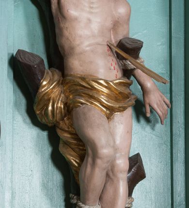 Zdjęcie nr 14: Nastawa ołtarzowa architektoniczna, jednokondygnacyjna, trójosiowa ze zwieńczeniem i z bramkami. Ołtarz prostopadłościenny, drewniany, mensa drewniana z kamiennym portatylem. Antependium w formie leżącego prostokąta ujętego złoconą, profilowaną ramą. W polu obraz malowany olejem na płótnie. W centrum kartusz w kształcie wydłużonego czwórliścia, dekorowany muszlą i wolutami z przedstawieniem pejzażu i widokiem na Golgotę. Po bokach kartusza bujne gałązki kwiatów. Tabernakulum w formie prostopadłościennej skrzynki o wypukłej ścianie frontowej, na profilowanym cokole, zamknięte profilowanym gzymsem, ujęte uszami utworzonymi z liści. Nad drzwiczkami, na gzymsie kartusz z niewielkim krucyfiksem. Powyżej tron wystawienia w formie profilowanej podstawy dekorowanej liśćmi. Na ściance frontowej tabernakulum profilowana rama w kształcie stojącego prostokąta zamkniętego łukiem nadwieszonym, w polu drzwiczki w formie stojącego prostokąta z przedstawieniem kielicha w glorii, powyżej drzwiczek winne grono. 

Nastawa ustawiona na zdwojonym cokole, dekorowanym wijącym się akantem. Osie kondygnacji wydzielone dwiema parami pilastrów oraz ustawionymi ukośnie kolumnami. Podpory dźwigają pełne belkowanie, przerwane nad polem środkowym i wyłamane nad osiami bocznymi, na których skraju ustawiony jest ukośnie przerwany, wolutowy przyczółek. Kolumny o kręconych trzonach, owinięte wicią liści akantu, kapitele korynckie; imposty ustawione pod kątem. W polu środkowym rama w kształcie stojącego prostokąta zamkniętego łukiem półkolistym z obrazem św. Kwiryna. W osiach bocznych płytkie płyciny, zwieńczone konchą z figurami św. Sebastiana po lewej stronie i św. Jana Nepomucena po prawej stronie, ustawionymi na wspornikach. Kondygnacja ujęta jest po bokach szerokimi uszami utworzonymi z liści akantu i karbowanej wstęgi. Fryz nad osiami bocznymi zdobiony kartuszami, we fryzie impostów z dwóch stron rozety; przyłucza osi bocznych dekorowane akantem.

W zwieńczeniu rzeźbiona półpostać Boga Ojca na obłoku z widocznym poniżej fragmentem globu ziemskiego i gołębicą Ducha Świętego; całość ukazana na tle promienistej glorii. Na belkowaniu, na osiach podpór wewnętrznych ustawione są rzeźby: św. Rocha  po lewej stronie i św. Wawrzyńca po prawej, a na zewnętrznych osiach retabulum rzeźby: Karola Boromeusza po lewej stronie i św. Stefana po prawej.

Nastawa ołtarzowa ujęta jest po bokach szerokimi bramkami w kształcie stojących prostokątów z drzwiczkami zamkniętymi półkoliście. Bramki ujęte są pilastrami o kanelowanych trzonach i fantazyjnych kapitelach, wspierających niepełne belkowanie oraz przerwany przyczółek. Nad bramkami ustawione są na cokołach rzeźby: św. Piotra po lewej stronie i św. Pawła po prawej. W polu drzwiczek owalne kartusze z herbem Görgey. W prawym kartuszu opisanym słowami: „BALTHAZAR GÖRGEI SENIOR”. Nad arkadami bramek są muszle, w przyłuczach akant, we fryzie rozety, a przerwany przyczółek dekorowany jest akantem. Struktura w całości polichromowana w odcieniu bladozielonym; ornamentyka, kolumny i profilowania złocone, detale srebrzone.