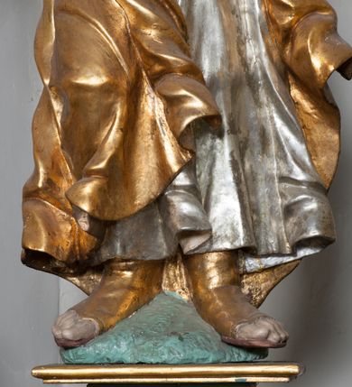 Zdjęcie nr 30: Nastawa ołtarzowa architektoniczna, jednokondygnacyjna, trójosiowa ze zwieńczeniem i z bramkami. Ołtarz prostopadłościenny, drewniany, mensa drewniana z kamiennym portatylem. Antependium w formie leżącego prostokąta ujętego złoconą, profilowaną ramą. W polu obraz malowany olejem na płótnie. W centrum kartusz w kształcie wydłużonego czwórliścia, dekorowany muszlą i wolutami z przedstawieniem pejzażu i widokiem na Golgotę. Po bokach kartusza bujne gałązki kwiatów. Tabernakulum w formie prostopadłościennej skrzynki o wypukłej ścianie frontowej, na profilowanym cokole, zamknięte profilowanym gzymsem, ujęte uszami utworzonymi z liści. Nad drzwiczkami, na gzymsie kartusz z niewielkim krucyfiksem. Powyżej tron wystawienia w formie profilowanej podstawy dekorowanej liśćmi. Na ściance frontowej tabernakulum profilowana rama w kształcie stojącego prostokąta zamkniętego łukiem nadwieszonym, w polu drzwiczki w formie stojącego prostokąta z przedstawieniem kielicha w glorii, powyżej drzwiczek winne grono. 

Nastawa ustawiona na zdwojonym cokole, dekorowanym wijącym się akantem. Osie kondygnacji wydzielone dwiema parami pilastrów oraz ustawionymi ukośnie kolumnami. Podpory dźwigają pełne belkowanie, przerwane nad polem środkowym i wyłamane nad osiami bocznymi, na których skraju ustawiony jest ukośnie przerwany, wolutowy przyczółek. Kolumny o kręconych trzonach, owinięte wicią liści akantu, kapitele korynckie; imposty ustawione pod kątem. W polu środkowym rama w kształcie stojącego prostokąta zamkniętego łukiem półkolistym z obrazem św. Kwiryna. W osiach bocznych płytkie płyciny, zwieńczone konchą z figurami św. Sebastiana po lewej stronie i św. Jana Nepomucena po prawej stronie, ustawionymi na wspornikach. Kondygnacja ujęta jest po bokach szerokimi uszami utworzonymi z liści akantu i karbowanej wstęgi. Fryz nad osiami bocznymi zdobiony kartuszami, we fryzie impostów z dwóch stron rozety; przyłucza osi bocznych dekorowane akantem.

W zwieńczeniu rzeźbiona półpostać Boga Ojca na obłoku z widocznym poniżej fragmentem globu ziemskiego i gołębicą Ducha Świętego; całość ukazana na tle promienistej glorii. Na belkowaniu, na osiach podpór wewnętrznych ustawione są rzeźby: św. Rocha  po lewej stronie i św. Wawrzyńca po prawej, a na zewnętrznych osiach retabulum rzeźby: Karola Boromeusza po lewej stronie i św. Stefana po prawej.

Nastawa ołtarzowa ujęta jest po bokach szerokimi bramkami w kształcie stojących prostokątów z drzwiczkami zamkniętymi półkoliście. Bramki ujęte są pilastrami o kanelowanych trzonach i fantazyjnych kapitelach, wspierających niepełne belkowanie oraz przerwany przyczółek. Nad bramkami ustawione są na cokołach rzeźby: św. Piotra po lewej stronie i św. Pawła po prawej. W polu drzwiczek owalne kartusze z herbem Görgey. W prawym kartuszu opisanym słowami: „BALTHAZAR GÖRGEI SENIOR”. Nad arkadami bramek są muszle, w przyłuczach akant, we fryzie rozety, a przerwany przyczółek dekorowany jest akantem. Struktura w całości polichromowana w odcieniu bladozielonym; ornamentyka, kolumny i profilowania złocone, detale srebrzone.