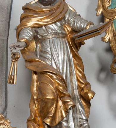 Zdjęcie nr 27: Nastawa ołtarzowa architektoniczna, jednokondygnacyjna, trójosiowa ze zwieńczeniem i z bramkami. Ołtarz prostopadłościenny, drewniany, mensa drewniana z kamiennym portatylem. Antependium w formie leżącego prostokąta ujętego złoconą, profilowaną ramą. W polu obraz malowany olejem na płótnie. W centrum kartusz w kształcie wydłużonego czwórliścia, dekorowany muszlą i wolutami z przedstawieniem pejzażu i widokiem na Golgotę. Po bokach kartusza bujne gałązki kwiatów. Tabernakulum w formie prostopadłościennej skrzynki o wypukłej ścianie frontowej, na profilowanym cokole, zamknięte profilowanym gzymsem, ujęte uszami utworzonymi z liści. Nad drzwiczkami, na gzymsie kartusz z niewielkim krucyfiksem. Powyżej tron wystawienia w formie profilowanej podstawy dekorowanej liśćmi. Na ściance frontowej tabernakulum profilowana rama w kształcie stojącego prostokąta zamkniętego łukiem nadwieszonym, w polu drzwiczki w formie stojącego prostokąta z przedstawieniem kielicha w glorii, powyżej drzwiczek winne grono. 

Nastawa ustawiona na zdwojonym cokole, dekorowanym wijącym się akantem. Osie kondygnacji wydzielone dwiema parami pilastrów oraz ustawionymi ukośnie kolumnami. Podpory dźwigają pełne belkowanie, przerwane nad polem środkowym i wyłamane nad osiami bocznymi, na których skraju ustawiony jest ukośnie przerwany, wolutowy przyczółek. Kolumny o kręconych trzonach, owinięte wicią liści akantu, kapitele korynckie; imposty ustawione pod kątem. W polu środkowym rama w kształcie stojącego prostokąta zamkniętego łukiem półkolistym z obrazem św. Kwiryna. W osiach bocznych płytkie płyciny, zwieńczone konchą z figurami św. Sebastiana po lewej stronie i św. Jana Nepomucena po prawej stronie, ustawionymi na wspornikach. Kondygnacja ujęta jest po bokach szerokimi uszami utworzonymi z liści akantu i karbowanej wstęgi. Fryz nad osiami bocznymi zdobiony kartuszami, we fryzie impostów z dwóch stron rozety; przyłucza osi bocznych dekorowane akantem.

W zwieńczeniu rzeźbiona półpostać Boga Ojca na obłoku z widocznym poniżej fragmentem globu ziemskiego i gołębicą Ducha Świętego; całość ukazana na tle promienistej glorii. Na belkowaniu, na osiach podpór wewnętrznych ustawione są rzeźby: św. Rocha  po lewej stronie i św. Wawrzyńca po prawej, a na zewnętrznych osiach retabulum rzeźby: Karola Boromeusza po lewej stronie i św. Stefana po prawej.

Nastawa ołtarzowa ujęta jest po bokach szerokimi bramkami w kształcie stojących prostokątów z drzwiczkami zamkniętymi półkoliście. Bramki ujęte są pilastrami o kanelowanych trzonach i fantazyjnych kapitelach, wspierających niepełne belkowanie oraz przerwany przyczółek. Nad bramkami ustawione są na cokołach rzeźby: św. Piotra po lewej stronie i św. Pawła po prawej. W polu drzwiczek owalne kartusze z herbem Görgey. W prawym kartuszu opisanym słowami: „BALTHAZAR GÖRGEI SENIOR”. Nad arkadami bramek są muszle, w przyłuczach akant, we fryzie rozety, a przerwany przyczółek dekorowany jest akantem. Struktura w całości polichromowana w odcieniu bladozielonym; ornamentyka, kolumny i profilowania złocone, detale srebrzone.