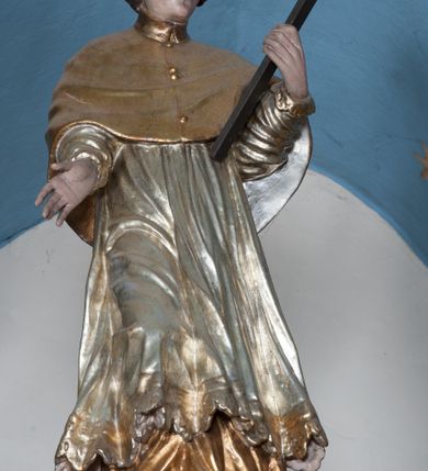 Zdjęcie nr 44: Nastawa ołtarzowa architektoniczna, jednokondygnacyjna, trójosiowa ze zwieńczeniem i z bramkami. Ołtarz prostopadłościenny, drewniany, mensa drewniana z kamiennym portatylem. Antependium w formie leżącego prostokąta ujętego złoconą, profilowaną ramą. W polu obraz malowany olejem na płótnie. W centrum kartusz w kształcie wydłużonego czwórliścia, dekorowany muszlą i wolutami z przedstawieniem pejzażu i widokiem na Golgotę. Po bokach kartusza bujne gałązki kwiatów. Tabernakulum w formie prostopadłościennej skrzynki o wypukłej ścianie frontowej, na profilowanym cokole, zamknięte profilowanym gzymsem, ujęte uszami utworzonymi z liści. Nad drzwiczkami, na gzymsie kartusz z niewielkim krucyfiksem. Powyżej tron wystawienia w formie profilowanej podstawy dekorowanej liśćmi. Na ściance frontowej tabernakulum profilowana rama w kształcie stojącego prostokąta zamkniętego łukiem nadwieszonym, w polu drzwiczki w formie stojącego prostokąta z przedstawieniem kielicha w glorii, powyżej drzwiczek winne grono. 

Nastawa ustawiona na zdwojonym cokole, dekorowanym wijącym się akantem. Osie kondygnacji wydzielone dwiema parami pilastrów oraz ustawionymi ukośnie kolumnami. Podpory dźwigają pełne belkowanie, przerwane nad polem środkowym i wyłamane nad osiami bocznymi, na których skraju ustawiony jest ukośnie przerwany, wolutowy przyczółek. Kolumny o kręconych trzonach, owinięte wicią liści akantu, kapitele korynckie; imposty ustawione pod kątem. W polu środkowym rama w kształcie stojącego prostokąta zamkniętego łukiem półkolistym z obrazem św. Kwiryna. W osiach bocznych płytkie płyciny, zwieńczone konchą z figurami św. Sebastiana po lewej stronie i św. Jana Nepomucena po prawej stronie, ustawionymi na wspornikach. Kondygnacja ujęta jest po bokach szerokimi uszami utworzonymi z liści akantu i karbowanej wstęgi. Fryz nad osiami bocznymi zdobiony kartuszami, we fryzie impostów z dwóch stron rozety; przyłucza osi bocznych dekorowane akantem.

W zwieńczeniu rzeźbiona półpostać Boga Ojca na obłoku z widocznym poniżej fragmentem globu ziemskiego i gołębicą Ducha Świętego; całość ukazana na tle promienistej glorii. Na belkowaniu, na osiach podpór wewnętrznych ustawione są rzeźby: św. Rocha  po lewej stronie i św. Wawrzyńca po prawej, a na zewnętrznych osiach retabulum rzeźby: Karola Boromeusza po lewej stronie i św. Stefana po prawej.

Nastawa ołtarzowa ujęta jest po bokach szerokimi bramkami w kształcie stojących prostokątów z drzwiczkami zamkniętymi półkoliście. Bramki ujęte są pilastrami o kanelowanych trzonach i fantazyjnych kapitelach, wspierających niepełne belkowanie oraz przerwany przyczółek. Nad bramkami ustawione są na cokołach rzeźby: św. Piotra po lewej stronie i św. Pawła po prawej. W polu drzwiczek owalne kartusze z herbem Görgey. W prawym kartuszu opisanym słowami: „BALTHAZAR GÖRGEI SENIOR”. Nad arkadami bramek są muszle, w przyłuczach akant, we fryzie rozety, a przerwany przyczółek dekorowany jest akantem. Struktura w całości polichromowana w odcieniu bladozielonym; ornamentyka, kolumny i profilowania złocone, detale srebrzone.