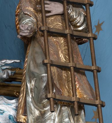 Zdjęcie nr 40: Nastawa ołtarzowa architektoniczna, jednokondygnacyjna, trójosiowa ze zwieńczeniem i z bramkami. Ołtarz prostopadłościenny, drewniany, mensa drewniana z kamiennym portatylem. Antependium w formie leżącego prostokąta ujętego złoconą, profilowaną ramą. W polu obraz malowany olejem na płótnie. W centrum kartusz w kształcie wydłużonego czwórliścia, dekorowany muszlą i wolutami z przedstawieniem pejzażu i widokiem na Golgotę. Po bokach kartusza bujne gałązki kwiatów. Tabernakulum w formie prostopadłościennej skrzynki o wypukłej ścianie frontowej, na profilowanym cokole, zamknięte profilowanym gzymsem, ujęte uszami utworzonymi z liści. Nad drzwiczkami, na gzymsie kartusz z niewielkim krucyfiksem. Powyżej tron wystawienia w formie profilowanej podstawy dekorowanej liśćmi. Na ściance frontowej tabernakulum profilowana rama w kształcie stojącego prostokąta zamkniętego łukiem nadwieszonym, w polu drzwiczki w formie stojącego prostokąta z przedstawieniem kielicha w glorii, powyżej drzwiczek winne grono. 

Nastawa ustawiona na zdwojonym cokole, dekorowanym wijącym się akantem. Osie kondygnacji wydzielone dwiema parami pilastrów oraz ustawionymi ukośnie kolumnami. Podpory dźwigają pełne belkowanie, przerwane nad polem środkowym i wyłamane nad osiami bocznymi, na których skraju ustawiony jest ukośnie przerwany, wolutowy przyczółek. Kolumny o kręconych trzonach, owinięte wicią liści akantu, kapitele korynckie; imposty ustawione pod kątem. W polu środkowym rama w kształcie stojącego prostokąta zamkniętego łukiem półkolistym z obrazem św. Kwiryna. W osiach bocznych płytkie płyciny, zwieńczone konchą z figurami św. Sebastiana po lewej stronie i św. Jana Nepomucena po prawej stronie, ustawionymi na wspornikach. Kondygnacja ujęta jest po bokach szerokimi uszami utworzonymi z liści akantu i karbowanej wstęgi. Fryz nad osiami bocznymi zdobiony kartuszami, we fryzie impostów z dwóch stron rozety; przyłucza osi bocznych dekorowane akantem.

W zwieńczeniu rzeźbiona półpostać Boga Ojca na obłoku z widocznym poniżej fragmentem globu ziemskiego i gołębicą Ducha Świętego; całość ukazana na tle promienistej glorii. Na belkowaniu, na osiach podpór wewnętrznych ustawione są rzeźby: św. Rocha  po lewej stronie i św. Wawrzyńca po prawej, a na zewnętrznych osiach retabulum rzeźby: Karola Boromeusza po lewej stronie i św. Stefana po prawej.

Nastawa ołtarzowa ujęta jest po bokach szerokimi bramkami w kształcie stojących prostokątów z drzwiczkami zamkniętymi półkoliście. Bramki ujęte są pilastrami o kanelowanych trzonach i fantazyjnych kapitelach, wspierających niepełne belkowanie oraz przerwany przyczółek. Nad bramkami ustawione są na cokołach rzeźby: św. Piotra po lewej stronie i św. Pawła po prawej. W polu drzwiczek owalne kartusze z herbem Görgey. W prawym kartuszu opisanym słowami: „BALTHAZAR GÖRGEI SENIOR”. Nad arkadami bramek są muszle, w przyłuczach akant, we fryzie rozety, a przerwany przyczółek dekorowany jest akantem. Struktura w całości polichromowana w odcieniu bladozielonym; ornamentyka, kolumny i profilowania złocone, detale srebrzone.