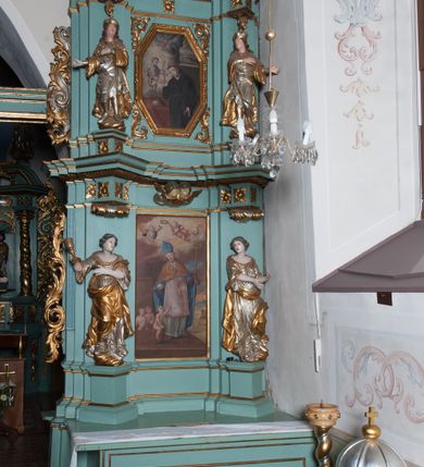 Zdjęcie nr 10: Ołtarz architektoniczny, dwukondygnacyjny, jednoosiowy. Ołtarz drewniany prostopadłościenny z drewnianą mensą i kamiennym portatylem. Dwukondygnacyjne retabulum ustawione na podwójnym i zdwojonym cokole, ujęte parą zdwojonych pilastrów wspierających wyłamujące się belkowanie. W polu głównym umieszczony jest obraz św. Mikołaja w płytkiej wnęce w kształcie stojącego prostokąta. Nad obrazem, w partii fryzu dwie uskrzydlone główki anielskie. Po bokach, na osi podpór, na wysokich cokołach ustawione są rzeźby: po lewej stronie św. Barbary, a po prawej według przekazów w literaturze św. Apolonii. Ponad nimi podwieszone ukośnie fragmenty fryzu ozdobione rozetami na ściankach bocznych, a od spodu szerokimi, zawiniętymi liśćmi akantu. Druga kondygnacja ustawiona na niskim cokole, ujęta parą zdwojonych pilastrów podtrzymujących przerwane belkowanie oraz wolutowy, odwrócony przyczółek, na którego szczycie usadzona jest para aniołków. W polu środkowym w ramie o kształcie stojącego prostokąta i ściętych narożach obraz św. Antoniego Padewskiego. Na osi podpór, na niskich cokołach ozdobionych rozetami ustawione są figury świętych królewiczów, zapewne. Ponad nimi podwieszone fragmenty fryzu, zdobione rozetami oraz z podwieszonymi szyszkami. Na szczycie retabulum niski cokolik, flankowany wolutami, zdobiony na przodzie rozetą z zatkniętym u góry krzyżem zakonu Bożogrobowców. Kondygnacje ujęte z lewej strony uszami: w dolnej suchym akantem, a w górnej akantem przeplecionym wstęgą, zdobioną cekinami. Kolorystyka struktury w kolorze jasnej zieleni, ornamentyka i detal architektoniczny złocone oraz srebrzone.
Napis na portatylu: „1963 d. 26 Jan. / celmus Ac erdemus Julianus / Groblicki, eppus tit philald / phiensis in arabia Auxil. Craco / ven, altare hoc portatile con / secravit et Reliquias Eses. Nn. /  brittcia rp. et florii in eo / inclusit” oraz podpisy piórem niebieskim oraz fragment pieczęci krakowskiej Bazyliki metropolitalnej.