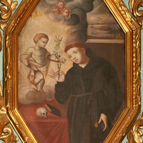 Zdjęcie nr 1: Obraz w kształcie wydłużonego, stojącego ośmioboku z przedstawieniem św. Antoniego, ukazanego w trzech czwartych do wysokości kolan. Święty zwrócony jest delikatnie w prawo, lewą rękę ma opuszczoną w dół, a w prawej ugiętej w łokciu trzyma kwiat lilii. Twarz pełna o delikatnych rysach z małymi oczami, na głowie tonsura. Ubrany jest w habit franciszkański, przewiązany cingulum z różańcem zawieszonym u lewego boku. Po lewej stronie kompozycji znajduje się stolik nakryty czerwonym obrusem, na którym leży czaszka i oparta o nią księga. Nad stolikiem na chmurze obłoków stoi zwrócone trzy czwarte w lewo Dzieciątko w rozświetlonej poświacie, które lewą dłonią chwyta gałązkę lilii, a prawą podtrzymuje płaszcz. Dzieciątko ma krótkie, kędzierzawe włosy. Ubrane jest w szatę, która odsłania nagi tors i nogi, przewieszoną przez ramiona i biegnącą na wysokości bioder. Powyżej na chmurze obłoków trzy uskrzydlone główki aniołków i jedna na skraju obłoków. Całość ukazana we wnętrzu architektonicznym z oknem po prawej stronie. Za oknem widok na port ze statkami i miastem w oddali. Rama drewniana, profilowana, zdobiona liśćmi wawrzynu. 