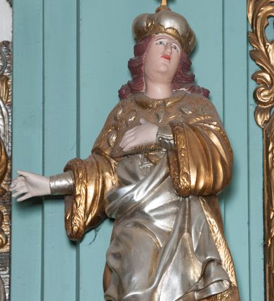 Zdjęcie nr 1: Rzeźba ścięta z tyłu, drążona, przedstawia nierozpoznanego, świętego królewicza. Figura ustawiona frontalnie, w delikatnym kontrapoście z prawą nogą ugiętą w kolanie, z głową uniesioną do góry. Obie ręce wyciągnięte w prawo. Twarz owalna z wyraźnie zaznaczonym podbródkiem, dużym nosem i małymi ustami. Włosy ciemne, długie, zasłaniające uszy i zawinięte dużymi lokami do tyłu. Święty ubrany jest w buty z wysokimi cholewami, srebrzoną suknię sięgającą do kolan z długimi rękawami, oraz złocony płaszcz królewski z gronostajowym podbiciem i pelerynką. Na głowie zamknięta korona. Polichromia naturalistyczna w odsłoniętych partiach ciała, strój i atrybuty złocone.

