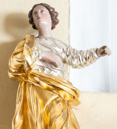 Zdjęcie nr 1: Rzeźba ścięta z tyłu przedstawiająca św. Marię Magdalenę. Święta ukazana w postawie stojącej w delikatnym kontrapoście z prawą dłonią złożoną na piersi i lewą wyciągniętą w bok. Twarz pełna z małymi ustami, długim nosem oraz wąskimi oczami. Włosy ciemne, średniej długości zawinięte do tyłu w bujne loki. 
Ubrana jest w srebrzoną suknię z długimi rękawami oraz złocony płaszcz przewieszony przez prawe ramię i spływający z przodu przez biodra. Na stopach ma brązowe buty. Polichromia w odsłoniętych partiach ciała naturalistyczna. 
