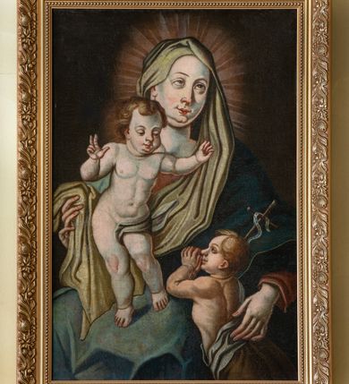 Zdjęcie nr 2: Obraz w kształcie stojącego prostokąta przedstawiający Matkę Boską z Dzieciątkiem i św. Janem Chrzcicielem. W centrum kompozycji ukazana Maria w ujęciu do kolan, w pozycji siedzącej, delikatnie zwrócona w lewo. Prawą dłonią obejmuje stojące na jej kolanach Dzieciątko, a lewą św. Jana Chrzciciela, który stoi po prawej stronie obrazu. Twarz Marii pełna o bladej karnacji z wyraźnie zaznaczonym podbródkiem, długim nosem oraz dużymi oczami ze wzrokiem skierowanym ku górze. Ubrana jest w czerwoną suknię z długimi rękawami, niebieski płaszcz oraz jasnozielony welon na głowie, którego jeden koniec przytrzymuje prawą dłonią. Wokół głowy Matki Boskiej jasne promienie. Dzieciątko ukazane w pozycji stojącej, w lekkim wykroku o esowato wygiętej sylwetce. Ręce ma uniesione, prawą dłonią czyni gest błogosławieństwa. Twarz pełna, okolona brązowymi i krótkimi włosami, oczy przymknięte, nos i usta niewielkie, wyraźnie zaznaczony podbródek. Dzieciątko ukazane niemal w akcie, z jasnoszarą chustą okrywającą lewe biodro. Po prawej stronie obrazu św. Jan Chrzciciel przedstawiony jako dziecko, zwrócony w stronę Dzieciątka Jezus. Ręce ma złożone i oparte na kolanach Marii, u prawego boku trzyma krzyż z białą banderolą. Głowa ukazana z lewego profilu, okolona jasnymi włosami z zadartym nosem i wyraźnym podbródkiem. Dół postaci okryty jasnobrązowym płaszczem z szarą podszewką. Rama nowa, drewniana, profilowana, fakturowana i złocona, od wewnątrz zdobiona perełkowaniem, a na zewnątrz wicią roślinną. Na odwrociu kartka z informacją: „Sponsorzy renowacji: / Beata i Andrzej Kuruc / Barbara i Jan Sołtys”.