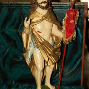 Zdjęcie nr 1: Rzeźba Chrystusa Zmartwychwstałego pełnoplastyczna, wolnostojąca. Chrystus ukazany jest w całej postaci, ustawiony frontalnie, w delikatnym kontrapoście; prawą, wysoko uniesioną ręką czyni gest błogosławieństwa, a w lewej trzyma chorągiew o długim drzewcu zakończonym krzyżem, na czerwonej tkaninie chorągwi widnieje złoty krzyż. Chrystus ma podłużną twarz z długim i wąskim nosem, wzrokiem skierowanym w dal oraz krótką i ciemną brodę, rozdzieloną na końcu w dwa pukle. Włosy długie i ciemnobrązowe, opadają na plecy i ramiona. Chrystus jest ubrany w złocony płaszcz spięty na piersi, z lewą połą przerzuconą przez prawą rękę. Na biodrach ma założone srebrzone perizonium. Na dłoniach, stopach i boku zaznaczone są ślady męki. Polichromia ciała jest naturalistyczna. Rzeźba ustawiona jest na niskiej podstawie w kształcie prostokąta o ściętych narożach, na którym osadzona jest zielona skała.