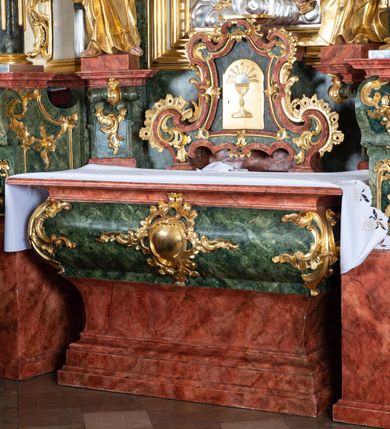 Zdjęcie nr 4: Ołtarz przyścienny, architektoniczny z mensą w formie sarkofagu o wklęsło-wypukłych bokach. W mensie kamienny portatyl. Retabulum jednoosiowe, jednokondygnacyjne ze zwieńczeniem, ustawione na wysokim zdwojonym cokole, zryzalitowanym bo bokach. Nastawa ujęta parą narożnych pilastrów kompozytowych oraz parą kolumn znacznie wysuniętych przed lico ołtarza. Kolumny o kanelowanych trzonach i kompozytowych głowicach podtrzymują faliste belkowanie. Zwieńczenie ujęte po bokach motywami „S” kształtnymi o wolutowo zwiniętych końcach, z których dolne mocno wysunięte do przodu, spoczywają na belkowaniu. Zwieńczenie zamknięte dwoma stykającymi się wolutami. Po bokach retabulum ażurowe uszaki formowane z grzebieni rocaille'owych i motywów „C” kształtnych z rzeźbioną, uskrzydloną główką anielską. 
Pole środkowe w kształcie prostokątnej wnęki z zamknięciem kształtowanym z motywów „C”. We wnęce płaskorzeźba z przedstawieniem Najświętszej Marii Panny Niepokalanie Poczętej ujęta podwójną profilowaną ramą. U dołu, po bokach wnęki dwie konsole z ustawionymi pełnoplastycznymi figurami św. Elżbiety po prawej oraz św. Anny po lewej stronie. Święta Elżbieta trzyma kartę z napisem: „IOANNES / EST / NOMEN / EIUS / Ann(…)”, a święta Anna otwartą księgę zapisaną słowami: „Merito igitur / germen eadem / Anaa divino germo reult / Spiritus pierna liberi libent / Labori qve durionustructa / Vertat am sancti ludaribusmais / Clamorite me cum opta / veram”. Ponad kolumnami, po bokach zwieńczenia dwie figury aniołów, powyżej para uskrzydlonych puttów. W zwieńczeniu owalna wnęka z obrazem przedstawiającym św. Jana Chrzciciela, ujętym podwójną ramą. 
Ołtarz bogato dekorowany. Mensa zdobiona ornamentem rocaille'owym. Pola cokołów zdobione płycinami kształtowanymi z grzebieni rocaille'owych dekorujących też fryz. Trzony kolumn i pilastrów zdobią podwieszane motywy rocaille'owe przeplatane z gałązkami róż, tworzącymi również rozległy, ażurowy kartusz nad polem środkowym. Boki zwieńczenia ujęte ażurowymi liśćmi akantu. Poniżej wnęki ażurowa, ukośna kratka regencyjna. Boki wnęki i szczyt zwieńczenia dekorowane pełnoplastycznymi rocaille'ami. 
Całość struktury ołtarza pokryta malowaną marmoryzacją w odcieniach zieleni i brązu. Detal architektoniczny złocony, pilastry srebrzone.