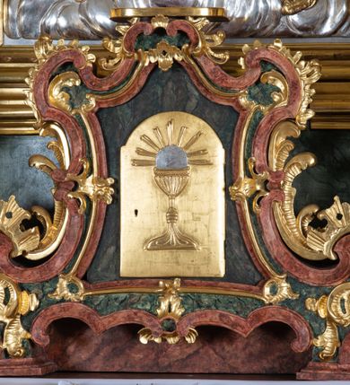 Zdjęcie nr 5: Ołtarz przyścienny, architektoniczny z mensą w formie sarkofagu o wklęsło-wypukłych bokach. W mensie kamienny portatyl. Retabulum jednoosiowe, jednokondygnacyjne ze zwieńczeniem, ustawione na wysokim zdwojonym cokole, zryzalitowanym bo bokach. Nastawa ujęta parą narożnych pilastrów kompozytowych oraz parą kolumn znacznie wysuniętych przed lico ołtarza. Kolumny o kanelowanych trzonach i kompozytowych głowicach podtrzymują faliste belkowanie. Zwieńczenie ujęte po bokach motywami „S” kształtnymi o wolutowo zwiniętych końcach, z których dolne mocno wysunięte do przodu, spoczywają na belkowaniu. Zwieńczenie zamknięte dwoma stykającymi się wolutami. Po bokach retabulum ażurowe uszaki formowane z grzebieni rocaille&#039;owych i motywów „C” kształtnych z rzeźbioną, uskrzydloną główką anielską. 
Pole środkowe w kształcie prostokątnej wnęki z zamknięciem kształtowanym z motywów „C”. We wnęce płaskorzeźba z przedstawieniem Najświętszej Marii Panny Niepokalanie Poczętej ujęta podwójną profilowaną ramą. U dołu, po bokach wnęki dwie konsole z ustawionymi pełnoplastycznymi figurami św. Elżbiety po prawej oraz św. Anny po lewej stronie. Święta Elżbieta trzyma kartę z napisem: „IOANNES / EST / NOMEN / EIUS / Ann(…)”, a święta Anna otwartą księgę zapisaną słowami: „Merito igitur / germen eadem / Anaa divino germo reult / Spiritus pierna liberi libent / Labori qve durionustructa / Vertat am sancti ludaribusmais / Clamorite me cum opta / veram”. Ponad kolumnami, po bokach zwieńczenia dwie figury aniołów, powyżej para uskrzydlonych puttów. W zwieńczeniu owalna wnęka z obrazem przedstawiającym św. Jana Chrzciciela, ujętym podwójną ramą. 
Ołtarz bogato dekorowany. Mensa zdobiona ornamentem rocaille&#039;owym. Pola cokołów zdobione płycinami kształtowanymi z grzebieni rocaille&#039;owych dekorujących też fryz. Trzony kolumn i pilastrów zdobią podwieszane motywy rocaille&#039;owe przeplatane z gałązkami róż, tworzącymi również rozległy, ażurowy kartusz nad polem środkowym. Boki zwieńczenia ujęte ażurowymi liśćmi akantu. Poniżej wnęki ażurowa, ukośna kratka regencyjna. Boki wnęki i szczyt zwieńczenia dekorowane pełnoplastycznymi rocaille&#039;ami. 
Całość struktury ołtarza pokryta malowaną marmoryzacją w odcieniach zieleni i brązu. Detal architektoniczny złocony, pilastry srebrzone.