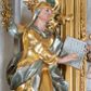 Zdjęcie nr 1: Rzeźba św. Anny ścięta z tyłu, drążona, ustawiona na prostopadłościennym, marmoryzowanym na jasnoczerwono cokole. Święta ukazana jest frontalnie w silnym kontrapoście z głową uniesioną ku górze. Ręce ma skierowane na lewy bok, trzyma w nich otwartą księgę zapisaną słowami: „Merito igitur / germen eadem / Anaa divino germo reult / Spiritus pierna liberi libent / Labori qve durionustructa / Vertat am sancti ludaribusmais / Clamorite me cum opta / veram”. Twarz szeroka o wyraźnie zaznaczonych kościach policzkowych, dużych oczach, małych ustach i nienaturalnie dużym nosie, policzki silnie zarumienione. Święta ubrana jest w długą suknię z długimi i wąskimi rękawami i gorsetem, drapowaną w grube fałdy. Na głowę ma nałożony złocony welon ze srebrzoną podszewką, a na lewe ramię złocony płaszcz ze srebrzoną podszewką, który zawija się z prawej strony ciała. Polichromia naturalistyczna w odsłoniętych partiach ciała; szaty i atrybuty złocone i srebrzone.
