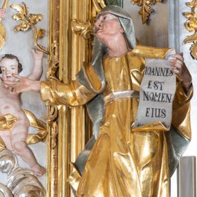 Zdjęcie nr 1: Rzeźba św. Elżbiety ścięta z tyłu, drążona, ustawiona na prostopadłościennym, marmoryzowanym na jasnoczerwono cokole. Święta jest ukazana frontalnie w silnym kontrapoście z głową uniesioną ku górze. Ręce ma rozłożone szeroko na boki, w lewej trzyma kartę z napisem: „IOANNES / EST / NOMEN / EIUS / Ann(?)”. Twarz szeroka o wyraźnie zaznaczonych kościach policzkowych, dużych oczach, małych ustach i nienaturalnie dużym nosie, policzki silnie zarumienione. Święta ubrana jest w długą suknię z długimi i wąskimi rękawami, przewiązaną w talli paskiem, drapowaną w grube i ostro łamane fałdy. Na głowę ma nałożony srebrzony welon. Polichromia naturalistyczna w odsłoniętych partiach ciała; szaty i atrybuty złocone i srebrzone.
