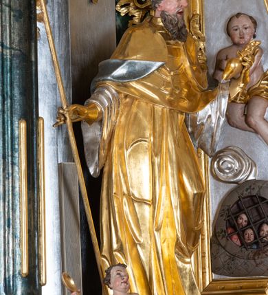 Zdjęcie nr 32: Ołtarz przyścienny, architektoniczny z mensą w formie sarkofagu o wklęsło-wypukłych bokach. W mensie kamienny portatyl. Retabulum jednoosiowe, jednokondygnacyjne ze zwieńczeniem, ustawione na wysokim zdwojonym cokole, zryzalitowanym bo bokach. Nastawa ujęta parą narożnych pilastrów kompozytowych oraz parą kolumn znacznie wysuniętych przed lico ołtarza. Kolumny o kanelowanych trzonach i kompozytowych głowicach podtrzymują faliste belkowanie. Zwieńczenie ujęte po bokach motywami „S” kształtnymi o wolutowo zwiniętych końcach, z których dolne mocno wysunięte do przodu, spoczywają na belkowaniu. Zwieńczenie zamknięte dwoma stykającymi się wolutami. Po bokach retabulum ażurowe uszaki formowane z grzebieni rocaille&#039;owych i motywów „C” kształtnych z rzeźbioną, uskrzydloną główką anielską. 
Pole środkowe w kształcie prostokątnej wnęki z zamknięciem kształtowanym z motywów „C”. We wnęce płaskorzeźba z przedstwieniem św. Mikołaja ujęta podwójną profilowaną ramą. U dołu, po bokach wnęki dwie konsole z ustawionymi pełnoplastycznymi figurami św. Augustyna po lewej oraz św. Marcina (?) po prawej stronie. Ponad kolumnami, po bokach zwieńczenia dwie figury aniołów, powyżej para uskrzydlonych puttów. W zwieńczeniu owalna wnęka z obrazem przedstawiającym św. Sebastiana, ujętym podwójną ramą. 
Ołtarz bogato dekorowany. Mensa zdobiona ornamentem rocaille&#039;owym. Pola cokołów zdobione płycinami kształtowanymi z grzebieni rocaille&#039;owych dekorujących też fryz. Trzony kolumn i pilastrów zdobią podwieszane motywy rocaille&#039;owe przeplatane z gałązkami róż, tworzącymi również rozległy, ażurowy kartusz nad polem środkowym. Boki zwieńczenia ujęte ażurowymi liśćmi akantu. Poniżej wnęki ażurowa, ukośna kratka regencyjna. Boki wnęki i szczyt zwieńczenia dekorowane pełnoplastycznymi rocaille&#039;ami. 
Całość struktury ołtarza pokryta malowaną marmoryzacją w odcieniach zieleni i brązu. Detal architektoniczny złocony, pilastry srebrzone.