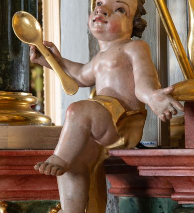 Zdjęcie nr 12: Ołtarz przyścienny, architektoniczny z mensą w formie sarkofagu o wklęsło-wypukłych bokach. W mensie kamienny portatyl. Retabulum jednoosiowe, jednokondygnacyjne ze zwieńczeniem, ustawione na wysokim zdwojonym cokole, zryzalitowanym bo bokach. Nastawa ujęta parą narożnych pilastrów kompozytowych oraz parą kolumn znacznie wysuniętych przed lico ołtarza. Kolumny o kanelowanych trzonach i kompozytowych głowicach podtrzymują faliste belkowanie. Zwieńczenie ujęte po bokach motywami „S” kształtnymi o wolutowo zwiniętych końcach, z których dolne mocno wysunięte do przodu, spoczywają na belkowaniu. Zwieńczenie zamknięte dwoma stykającymi się wolutami. Po bokach retabulum ażurowe uszaki formowane z grzebieni rocaille'owych i motywów „C” kształtnych z rzeźbioną, uskrzydloną główką anielską. 
Pole środkowe w kształcie prostokątnej wnęki z zamknięciem kształtowanym z motywów „C”. We wnęce płaskorzeźba z przedstwieniem św. Mikołaja ujęta podwójną profilowaną ramą. U dołu, po bokach wnęki dwie konsole z ustawionymi pełnoplastycznymi figurami św. Augustyna po lewej oraz św. Marcina (?) po prawej stronie. Ponad kolumnami, po bokach zwieńczenia dwie figury aniołów, powyżej para uskrzydlonych puttów. W zwieńczeniu owalna wnęka z obrazem przedstawiającym św. Sebastiana, ujętym podwójną ramą. 
Ołtarz bogato dekorowany. Mensa zdobiona ornamentem rocaille'owym. Pola cokołów zdobione płycinami kształtowanymi z grzebieni rocaille'owych dekorujących też fryz. Trzony kolumn i pilastrów zdobią podwieszane motywy rocaille'owe przeplatane z gałązkami róż, tworzącymi również rozległy, ażurowy kartusz nad polem środkowym. Boki zwieńczenia ujęte ażurowymi liśćmi akantu. Poniżej wnęki ażurowa, ukośna kratka regencyjna. Boki wnęki i szczyt zwieńczenia dekorowane pełnoplastycznymi rocaille'ami. 
Całość struktury ołtarza pokryta malowaną marmoryzacją w odcieniach zieleni i brązu. Detal architektoniczny złocony, pilastry srebrzone.