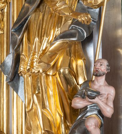 Zdjęcie nr 7: Ołtarz przyścienny, architektoniczny z mensą w formie sarkofagu o wklęsło-wypukłych bokach. W mensie kamienny portatyl. Retabulum jednoosiowe, jednokondygnacyjne ze zwieńczeniem, ustawione na wysokim zdwojonym cokole, zryzalitowanym bo bokach. Nastawa ujęta parą narożnych pilastrów kompozytowych oraz parą kolumn znacznie wysuniętych przed lico ołtarza. Kolumny o kanelowanych trzonach i kompozytowych głowicach podtrzymują faliste belkowanie. Zwieńczenie ujęte po bokach motywami „S” kształtnymi o wolutowo zwiniętych końcach, z których dolne mocno wysunięte do przodu, spoczywają na belkowaniu. Zwieńczenie zamknięte dwoma stykającymi się wolutami. Po bokach retabulum ażurowe uszaki formowane z grzebieni rocaille&#039;owych i motywów „C” kształtnych z rzeźbioną, uskrzydloną główką anielską. 
Pole środkowe w kształcie prostokątnej wnęki z zamknięciem kształtowanym z motywów „C”. We wnęce płaskorzeźba z przedstwieniem św. Mikołaja ujęta podwójną profilowaną ramą. U dołu, po bokach wnęki dwie konsole z ustawionymi pełnoplastycznymi figurami św. Augustyna po lewej oraz św. Marcina (?) po prawej stronie. Ponad kolumnami, po bokach zwieńczenia dwie figury aniołów, powyżej para uskrzydlonych puttów. W zwieńczeniu owalna wnęka z obrazem przedstawiającym św. Sebastiana, ujętym podwójną ramą. 
Ołtarz bogato dekorowany. Mensa zdobiona ornamentem rocaille&#039;owym. Pola cokołów zdobione płycinami kształtowanymi z grzebieni rocaille&#039;owych dekorujących też fryz. Trzony kolumn i pilastrów zdobią podwieszane motywy rocaille&#039;owe przeplatane z gałązkami róż, tworzącymi również rozległy, ażurowy kartusz nad polem środkowym. Boki zwieńczenia ujęte ażurowymi liśćmi akantu. Poniżej wnęki ażurowa, ukośna kratka regencyjna. Boki wnęki i szczyt zwieńczenia dekorowane pełnoplastycznymi rocaille&#039;ami. 
Całość struktury ołtarza pokryta malowaną marmoryzacją w odcieniach zieleni i brązu. Detal architektoniczny złocony, pilastry srebrzone.