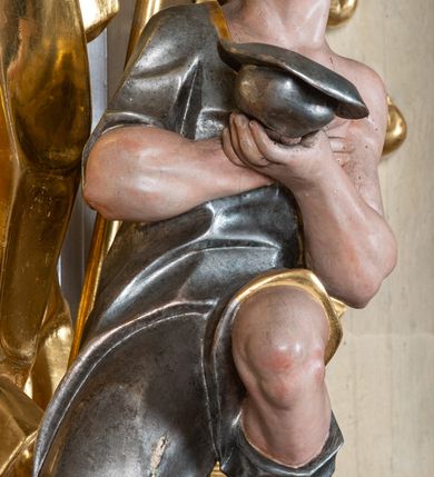 Zdjęcie nr 15: Ołtarz przyścienny, architektoniczny z mensą w formie sarkofagu o wklęsło-wypukłych bokach. W mensie kamienny portatyl. Retabulum jednoosiowe, jednokondygnacyjne ze zwieńczeniem, ustawione na wysokim zdwojonym cokole, zryzalitowanym bo bokach. Nastawa ujęta parą narożnych pilastrów kompozytowych oraz parą kolumn znacznie wysuniętych przed lico ołtarza. Kolumny o kanelowanych trzonach i kompozytowych głowicach podtrzymują faliste belkowanie. Zwieńczenie ujęte po bokach motywami „S” kształtnymi o wolutowo zwiniętych końcach, z których dolne mocno wysunięte do przodu, spoczywają na belkowaniu. Zwieńczenie zamknięte dwoma stykającymi się wolutami. Po bokach retabulum ażurowe uszaki formowane z grzebieni rocaille&#039;owych i motywów „C” kształtnych z rzeźbioną, uskrzydloną główką anielską. 
Pole środkowe w kształcie prostokątnej wnęki z zamknięciem kształtowanym z motywów „C”. We wnęce płaskorzeźba z przedstwieniem św. Mikołaja ujęta podwójną profilowaną ramą. U dołu, po bokach wnęki dwie konsole z ustawionymi pełnoplastycznymi figurami św. Augustyna po lewej oraz św. Marcina (?) po prawej stronie. Ponad kolumnami, po bokach zwieńczenia dwie figury aniołów, powyżej para uskrzydlonych puttów. W zwieńczeniu owalna wnęka z obrazem przedstawiającym św. Sebastiana, ujętym podwójną ramą. 
Ołtarz bogato dekorowany. Mensa zdobiona ornamentem rocaille&#039;owym. Pola cokołów zdobione płycinami kształtowanymi z grzebieni rocaille&#039;owych dekorujących też fryz. Trzony kolumn i pilastrów zdobią podwieszane motywy rocaille&#039;owe przeplatane z gałązkami róż, tworzącymi również rozległy, ażurowy kartusz nad polem środkowym. Boki zwieńczenia ujęte ażurowymi liśćmi akantu. Poniżej wnęki ażurowa, ukośna kratka regencyjna. Boki wnęki i szczyt zwieńczenia dekorowane pełnoplastycznymi rocaille&#039;ami. 
Całość struktury ołtarza pokryta malowaną marmoryzacją w odcieniach zieleni i brązu. Detal architektoniczny złocony, pilastry srebrzone.