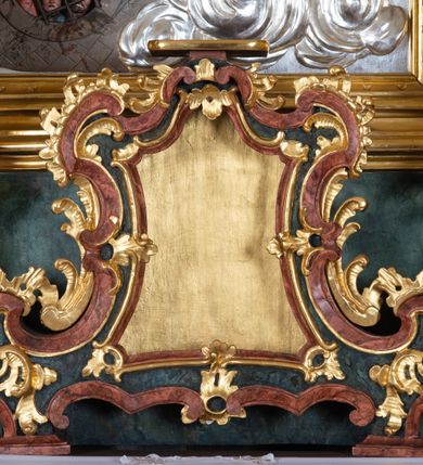 Zdjęcie nr 6: Ołtarz przyścienny, architektoniczny z mensą w formie sarkofagu o wklęsło-wypukłych bokach. W mensie kamienny portatyl. Retabulum jednoosiowe, jednokondygnacyjne ze zwieńczeniem, ustawione na wysokim zdwojonym cokole, zryzalitowanym bo bokach. Nastawa ujęta parą narożnych pilastrów kompozytowych oraz parą kolumn znacznie wysuniętych przed lico ołtarza. Kolumny o kanelowanych trzonach i kompozytowych głowicach podtrzymują faliste belkowanie. Zwieńczenie ujęte po bokach motywami „S” kształtnymi o wolutowo zwiniętych końcach, z których dolne mocno wysunięte do przodu, spoczywają na belkowaniu. Zwieńczenie zamknięte dwoma stykającymi się wolutami. Po bokach retabulum ażurowe uszaki formowane z grzebieni rocaille&#039;owych i motywów „C” kształtnych z rzeźbioną, uskrzydloną główką anielską. 
Pole środkowe w kształcie prostokątnej wnęki z zamknięciem kształtowanym z motywów „C”. We wnęce płaskorzeźba z przedstwieniem św. Mikołaja ujęta podwójną profilowaną ramą. U dołu, po bokach wnęki dwie konsole z ustawionymi pełnoplastycznymi figurami św. Augustyna po lewej oraz św. Marcina (?) po prawej stronie. Ponad kolumnami, po bokach zwieńczenia dwie figury aniołów, powyżej para uskrzydlonych puttów. W zwieńczeniu owalna wnęka z obrazem przedstawiającym św. Sebastiana, ujętym podwójną ramą. 
Ołtarz bogato dekorowany. Mensa zdobiona ornamentem rocaille&#039;owym. Pola cokołów zdobione płycinami kształtowanymi z grzebieni rocaille&#039;owych dekorujących też fryz. Trzony kolumn i pilastrów zdobią podwieszane motywy rocaille&#039;owe przeplatane z gałązkami róż, tworzącymi również rozległy, ażurowy kartusz nad polem środkowym. Boki zwieńczenia ujęte ażurowymi liśćmi akantu. Poniżej wnęki ażurowa, ukośna kratka regencyjna. Boki wnęki i szczyt zwieńczenia dekorowane pełnoplastycznymi rocaille&#039;ami. 
Całość struktury ołtarza pokryta malowaną marmoryzacją w odcieniach zieleni i brązu. Detal architektoniczny złocony, pilastry srebrzone.