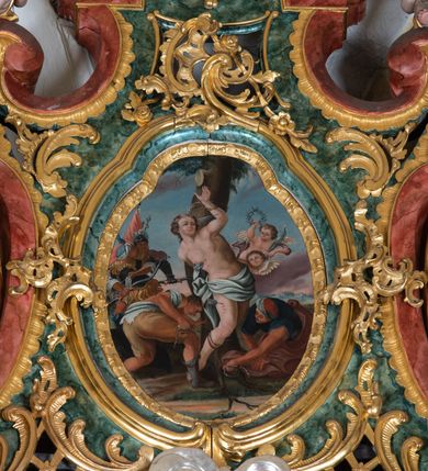 Zdjęcie nr 3: Ołtarz przyścienny, architektoniczny z mensą w formie sarkofagu o wklęsło-wypukłych bokach. W mensie kamienny portatyl. Retabulum jednoosiowe, jednokondygnacyjne ze zwieńczeniem, ustawione na wysokim zdwojonym cokole, zryzalitowanym bo bokach. Nastawa ujęta parą narożnych pilastrów kompozytowych oraz parą kolumn znacznie wysuniętych przed lico ołtarza. Kolumny o kanelowanych trzonach i kompozytowych głowicach podtrzymują faliste belkowanie. Zwieńczenie ujęte po bokach motywami „S” kształtnymi o wolutowo zwiniętych końcach, z których dolne mocno wysunięte do przodu, spoczywają na belkowaniu. Zwieńczenie zamknięte dwoma stykającymi się wolutami. Po bokach retabulum ażurowe uszaki formowane z grzebieni rocaille'owych i motywów „C” kształtnych z rzeźbioną, uskrzydloną główką anielską. 
Pole środkowe w kształcie prostokątnej wnęki z zamknięciem kształtowanym z motywów „C”. We wnęce płaskorzeźba z przedstwieniem św. Mikołaja ujęta podwójną profilowaną ramą. U dołu, po bokach wnęki dwie konsole z ustawionymi pełnoplastycznymi figurami św. Augustyna po lewej oraz św. Marcina (?) po prawej stronie. Ponad kolumnami, po bokach zwieńczenia dwie figury aniołów, powyżej para uskrzydlonych puttów. W zwieńczeniu owalna wnęka z obrazem przedstawiającym św. Sebastiana, ujętym podwójną ramą. 
Ołtarz bogato dekorowany. Mensa zdobiona ornamentem rocaille'owym. Pola cokołów zdobione płycinami kształtowanymi z grzebieni rocaille'owych dekorujących też fryz. Trzony kolumn i pilastrów zdobią podwieszane motywy rocaille'owe przeplatane z gałązkami róż, tworzącymi również rozległy, ażurowy kartusz nad polem środkowym. Boki zwieńczenia ujęte ażurowymi liśćmi akantu. Poniżej wnęki ażurowa, ukośna kratka regencyjna. Boki wnęki i szczyt zwieńczenia dekorowane pełnoplastycznymi rocaille'ami. 
Całość struktury ołtarza pokryta malowaną marmoryzacją w odcieniach zieleni i brązu. Detal architektoniczny złocony, pilastry srebrzone.