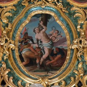 Zdjęcie nr 1: Obraz w kształcie owalu o wybrzuszonej górnej części przedstawiający św. Sebastiana przywiązanego do drzewa. Święty ukazany o silnie skręconej sylwetce z lewą ręką przywiązaną do drzewa nad głową, a prawą z tyłu pleców. Jego ciało przebite jest trzema strzałami. Twarz szeroka z krótkim nosem i małymi ustami oraz dużymi oczami ze wzrokiem skierowanym ku górze. Włosy długie, brązowe, falowane i upięte z tyłu. Święty ubrany jest w białą tkaninę opasającą biodra. Ciało o silnie podkreślonej muskulaturze i jasnej karnacji. Poniżej dwaj pochyleni oprawcy, którzy przywiązują świętego do drzewa. Mężczyzna po prawej ubrany jest w szare buty z wysokimi cholewami, krótkie i brązowe spodnie oraz białą chustę zarzuconą na plecy. Drugi oprawca ubrany jest w niebieską koszulę z krótkimi rękawami, jasnofioletowy płaszcz oraz orientalną czapkę na głowie. Po lewej stronie ukazani są kolejni dwaj oprawcy w pozycji stojącej, ubrani w stroje żołnierzy rzymskich, którzy w dłoniach trzymają włócznie i strzały. W oddali widać czerwoną chorągiew oraz dwie włócznie. Po prawej stronie obrazu półnagie putto z wieńcem chwały w prawej dłoni i palmą męczeństwa w lewej. Poniżej uskrzydlona główka anielska. W tle pejzaż górski i różowo-błękitne niebo. 