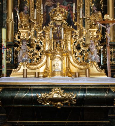 Zdjęcie nr 37: Nastawa ołtarzowa architektoniczna, trójosiowa z bramkami, jednokondygnacyjna ze zwieńczeniem. Ołtarz wysunięty do przodu, drewniany, sarkofagowy, wklęsło-wypukły, zwężający się ku dołowi, na profilowanym cokole, ujęty spływami wolutowymi; dekorowany w narożach palmetami, na froncie rocaille'owy kartusz z malowanymi skrzyżowanymi kluczami w polu. Mensa drewniana z silnie wysuniętą, profilowaną krawędzią, z portatylem z piaskowca. 

Tabernakulum w formie prostopadłościennej skrzynki o wypukłej ściance frontowej, ujęte z przodu ukośnie dostawionymi pilastrami na cokołach z trzonami w formie wolut, dźwigającymi niepełne belkowanie, opasujące je z trzech stron, nad ścianką frontową przyjmujące falistą formę zwieńczoną rocaille'm. Drzwiczki przyjmują kształt stojącego prostokąta zamkniętego łukiem półkolistym nadwieszonym, ujęte profilowaną ramą; w polu płaskorzeźbione przedstawienie kielicha z hostią w glorii na fakturowanym tle. Na belkowaniu, na osi podpór ustawiona jest para rocaille'owych lichtarzy. Tron wystawienia architektoniczny, trójosiowy; oś środkowa ponad tabernakulum w postaci ażurowej niszy z cokołem na pasyjkę, tylna ścianka utworzona z rocaille'u z kłosami zbóż; flankowana pilastrami zwieńczonymi falistym gzymsem, dźwigającymi ażurową, zamkniętą koronę. Podpory przechodzą w spływy wolutowe, ujmujące tabernakulum, na których końcach siedzi para adorujących puttów. Osie boczne są ujęte po bokach pilastrami dźwigającymi imposty podtrzymywane przez rocaille w partii trzonów oraz płonące wazony; pola wypełnione ażurowym rocaille'm i palmetami przechodzącymi w podwójne lichtarze.

Retabulum na planie półowalu, osie boczne ustawione prostopadle do środkowej. Oś środkowa posadowiona na wysokim, dwustrefowym cokole. W pierwszej strefie cokołu prostokątna płycina z napisem: „Z INICJATYWY / KS. PROBOSZCZA ROMANA GORCZYŃSKIEGO / W LATACH 2001 - 2006 / WYKONANO REMONT KOŚCIOŁA I KONSERWACJĘ / WYPOSAŻENIA”. W drugiej strefie cokołu, pośrodku płycina w formie leżącego prostokąta o fantazyjnie wyciętych bokach z malowanym kartuszem herbowym, dzielonym na cztery pola. W lewym górnym polu kartusza umieszczony jest orzeł, poniżej dwójka dzieci w łódce, a po prawej stronie tarczy, w prawym górnym polu dwójka dzieci w łódce, poniżej orzeł. U spodu napis z chronostychem: „EREXIT, AC EXORNAVIT HONORIBVS SANCTI PETRI, / AC PAVLI APOSTOLI ILLVSTRISSIMVS LIBER BAR I WNBS(?) IOANELLY / A TOLVANA PROPPII X I”. Klejnotem jest hełm z pióropuszem zakończony półpostacią rycerza w zbroi, zaś labry mają formę bujnej wici akantowej.  Ryzality cokołów ozdobione są z trzech stron rocaille'owymi płycinami; skrajne konsole rocaille'm i różanymi gałązkami. Oś główna flankowana parą kolumn ustawioną na tle zwielokrotnionych pilastrów. Podpory dźwigają pełne belkowanie, przerwane nad polem środkowym, wyłamane na ich osi oraz przerwany wolutowy przyczółek. W polu środkowym podwójna, profilowana rama w formie stojącego prostokąta zamkniętego łukiem nadwieszonym z uskokami z obrazem św. Piotra i św. Pawła; flankowana przez figury św. Szymona po lewej stronie i św. Judy Tadeusza po prawej, ustawionymi na rocaille'owych wspornikach. Ramy obrazu, trzony wewnętrznych pilastrów i pola za środkową parą figur dekorowane rocaille'm. 

Zwieńczenie w formie zbliżonej do stojącego prostokąta, ujęte spływami wolutowymi, zamknięte falistym gzymsem przechodzącym w antytetycznie zwrócone woluty. Całość zwieńczona gołębicą Ducha Świętego w glorii promienistej. W polu rzeźbiarska grupa Koronacji Marii w glorii promienistej, pośród obłoków i uskrzydlonych główek anielskich. Dwa flankujące grupę putta  na obłokach trzymają banderole z napisem: „FILIA DEI PATRIS” i „MATER DEI FILII”, a kolejne dwa usadzone na szczycie: „VENI CORONABERIS” oraz „VENI SPONSA MEA”. Poniżej zwieńczenia w ażurowym kartuszu znajduje się napis: „QVA E/ST ISTA / QVAE PROGREDI/TUR QVASI AURORA / CONSURGENS / Cant 6.”. Na przyczółku siedzące figury św. Joachima po lewej stronie i św. Józefa po prawej, na gzymsie flankującym pole środkowe dwa putta trzymające słońce i księżyc, na zewnętrznych osiach dwa adorujące anioły. Spływy zwieńczenia dekorowane strzępiastymi liśćmi palmowymi, muszlą i rocaille’m. 

Osie boczne ustawione są na wysokim cokole, od zewnątrz ujęte pilastrami przechodzącymi w woluty, od wewnątrz sąsiadują z osią środkową. Pośrodku bramki z drzwiczkami zakończonymi gzymsem przyjmującym formę cokołu dla figur. Drzwiczki w formie stojącego prostokątna zamkniętego łukiem segmentowym nadwieszonym; osie na skraju ujęte konsolami stanowiącymi cokoły dla podpór. Ryzalit bramek zdobiony płyciną ze strzępiastym grzebieniem; drzwiczki z płyciną z rocaille'm i kwiatowym zwisem na wstążce; powyższy cokół ujęty liśćmi palmowymi i rocaille'm. Kondygnacja flankowana na skraju kolumną ustawioną na tle pilastru, które podtrzymują wyłamany gzyms zakończony wolutami ujmującymi szczyt o falistym przebiegu, na którym ustawiony jest duży płomienisty wazon. W polach ustawione są figury: po lewej się Jakuba Starszego, a po prawej św. Filipa. Na zwieńczeniach usadzone dwie figury aniołów. 

Struktura w całości marmoryzowana w kolorze zielono-brązowym; ornamentyka, kolumny złocone, detale srebrzone. Wszystkie kolumny w jednej trzeciej wysokości przedzielone rocaille’m, a fryz z elementami dekoracji rokokowej. Tabernakulum i tron wystawienia w całości złocone.

