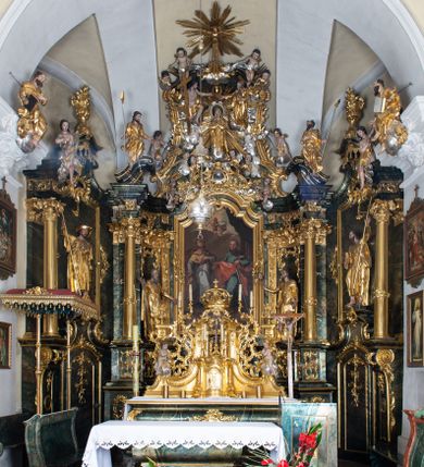 Zdjęcie nr 1: Nastawa ołtarzowa architektoniczna, trójosiowa z bramkami, jednokondygnacyjna ze zwieńczeniem. Ołtarz wysunięty do przodu, drewniany, sarkofagowy, wklęsło-wypukły, zwężający się ku dołowi, na profilowanym cokole, ujęty spływami wolutowymi; dekorowany w narożach palmetami, na froncie rocaille'owy kartusz z malowanymi skrzyżowanymi kluczami w polu. Mensa drewniana z silnie wysuniętą, profilowaną krawędzią, z portatylem z piaskowca. 

Tabernakulum w formie prostopadłościennej skrzynki o wypukłej ściance frontowej, ujęte z przodu ukośnie dostawionymi pilastrami na cokołach z trzonami w formie wolut, dźwigającymi niepełne belkowanie, opasujące je z trzech stron, nad ścianką frontową przyjmujące falistą formę zwieńczoną rocaille'm. Drzwiczki przyjmują kształt stojącego prostokąta zamkniętego łukiem półkolistym nadwieszonym, ujęte profilowaną ramą; w polu płaskorzeźbione przedstawienie kielicha z hostią w glorii na fakturowanym tle. Na belkowaniu, na osi podpór ustawiona jest para rocaille'owych lichtarzy. Tron wystawienia architektoniczny, trójosiowy; oś środkowa ponad tabernakulum w postaci ażurowej niszy z cokołem na pasyjkę, tylna ścianka utworzona z rocaille'u z kłosami zbóż; flankowana pilastrami zwieńczonymi falistym gzymsem, dźwigającymi ażurową, zamkniętą koronę. Podpory przechodzą w spływy wolutowe, ujmujące tabernakulum, na których końcach siedzi para adorujących puttów. Osie boczne są ujęte po bokach pilastrami dźwigającymi imposty podtrzymywane przez rocaille w partii trzonów oraz płonące wazony; pola wypełnione ażurowym rocaille'm i palmetami przechodzącymi w podwójne lichtarze.

Retabulum na planie półowalu, osie boczne ustawione prostopadle do środkowej. Oś środkowa posadowiona na wysokim, dwustrefowym cokole. W pierwszej strefie cokołu prostokątna płycina z napisem: „Z INICJATYWY / KS. PROBOSZCZA ROMANA GORCZYŃSKIEGO / W LATACH 2001 - 2006 / WYKONANO REMONT KOŚCIOŁA I KONSERWACJĘ / WYPOSAŻENIA”. W drugiej strefie cokołu, pośrodku płycina w formie leżącego prostokąta o fantazyjnie wyciętych bokach z malowanym kartuszem herbowym, dzielonym na cztery pola. W lewym górnym polu kartusza umieszczony jest orzeł, poniżej dwójka dzieci w łódce, a po prawej stronie tarczy, w prawym górnym polu dwójka dzieci w łódce, poniżej orzeł. U spodu napis z chronostychem: „EREXIT, AC EXORNAVIT HONORIBVS SANCTI PETRI, / AC PAVLI APOSTOLI ILLVSTRISSIMVS LIBER BAR I WNBS(?) IOANELLY / A TOLVANA PROPPII X I”. Klejnotem jest hełm z pióropuszem zakończony półpostacią rycerza w zbroi, zaś labry mają formę bujnej wici akantowej.  Ryzality cokołów ozdobione są z trzech stron rocaille'owymi płycinami; skrajne konsole rocaille'm i różanymi gałązkami. Oś główna flankowana parą kolumn ustawioną na tle zwielokrotnionych pilastrów. Podpory dźwigają pełne belkowanie, przerwane nad polem środkowym, wyłamane na ich osi oraz przerwany wolutowy przyczółek. W polu środkowym podwójna, profilowana rama w formie stojącego prostokąta zamkniętego łukiem nadwieszonym z uskokami z obrazem św. Piotra i św. Pawła; flankowana przez figury św. Szymona po lewej stronie i św. Judy Tadeusza po prawej, ustawionymi na rocaille'owych wspornikach. Ramy obrazu, trzony wewnętrznych pilastrów i pola za środkową parą figur dekorowane rocaille'm. 

Zwieńczenie w formie zbliżonej do stojącego prostokąta, ujęte spływami wolutowymi, zamknięte falistym gzymsem przechodzącym w antytetycznie zwrócone woluty. Całość zwieńczona gołębicą Ducha Świętego w glorii promienistej. W polu rzeźbiarska grupa Koronacji Marii w glorii promienistej, pośród obłoków i uskrzydlonych główek anielskich. Dwa flankujące grupę putta  na obłokach trzymają banderole z napisem: „FILIA DEI PATRIS” i „MATER DEI FILII”, a kolejne dwa usadzone na szczycie: „VENI CORONABERIS” oraz „VENI SPONSA MEA”. Poniżej zwieńczenia w ażurowym kartuszu znajduje się napis: „QVA E/ST ISTA / QVAE PROGREDI/TUR QVASI AURORA / CONSURGENS / Cant 6.”. Na przyczółku siedzące figury św. Joachima po lewej stronie i św. Józefa po prawej, na gzymsie flankującym pole środkowe dwa putta trzymające słońce i księżyc, na zewnętrznych osiach dwa adorujące anioły. Spływy zwieńczenia dekorowane strzępiastymi liśćmi palmowymi, muszlą i rocaille’m. 

Osie boczne ustawione są na wysokim cokole, od zewnątrz ujęte pilastrami przechodzącymi w woluty, od wewnątrz sąsiadują z osią środkową. Pośrodku bramki z drzwiczkami zakończonymi gzymsem przyjmującym formę cokołu dla figur. Drzwiczki w formie stojącego prostokątna zamkniętego łukiem segmentowym nadwieszonym; osie na skraju ujęte konsolami stanowiącymi cokoły dla podpór. Ryzalit bramek zdobiony płyciną ze strzępiastym grzebieniem; drzwiczki z płyciną z rocaille'm i kwiatowym zwisem na wstążce; powyższy cokół ujęty liśćmi palmowymi i rocaille'm. Kondygnacja flankowana na skraju kolumną ustawioną na tle pilastru, które podtrzymują wyłamany gzyms zakończony wolutami ujmującymi szczyt o falistym przebiegu, na którym ustawiony jest duży płomienisty wazon. W polach ustawione są figury: po lewej się Jakuba Starszego, a po prawej św. Filipa. Na zwieńczeniach usadzone dwie figury aniołów. 

Struktura w całości marmoryzowana w kolorze zielono-brązowym; ornamentyka, kolumny złocone, detale srebrzone. Wszystkie kolumny w jednej trzeciej wysokości przedzielone rocaille’m, a fryz z elementami dekoracji rokokowej. Tabernakulum i tron wystawienia w całości złocone.

