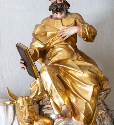 Zdjęcie nr 32: Nastawa ołtarzowa architektoniczna, trójosiowa z bramkami, jednokondygnacyjna ze zwieńczeniem. Ołtarz wysunięty do przodu, drewniany, sarkofagowy, wklęsło-wypukły, zwężający się ku dołowi, na profilowanym cokole, ujęty spływami wolutowymi; dekorowany w narożach palmetami, na froncie rocaille&#039;owy kartusz z malowanymi skrzyżowanymi kluczami w polu. Mensa drewniana z silnie wysuniętą, profilowaną krawędzią, z portatylem z piaskowca. 

Tabernakulum w formie prostopadłościennej skrzynki o wypukłej ściance frontowej, ujęte z przodu ukośnie dostawionymi pilastrami na cokołach z trzonami w formie wolut, dźwigającymi niepełne belkowanie, opasujące je z trzech stron, nad ścianką frontową przyjmujące falistą formę zwieńczoną rocaille&#039;m. Drzwiczki przyjmują kształt stojącego prostokąta zamkniętego łukiem półkolistym nadwieszonym, ujęte profilowaną ramą; w polu płaskorzeźbione przedstawienie kielicha z hostią w glorii na fakturowanym tle. Na belkowaniu, na osi podpór ustawiona jest para rocaille&#039;owych lichtarzy. Tron wystawienia architektoniczny, trójosiowy; oś środkowa ponad tabernakulum w postaci ażurowej niszy z cokołem na pasyjkę, tylna ścianka utworzona z rocaille&#039;u z kłosami zbóż; flankowana pilastrami zwieńczonymi falistym gzymsem, dźwigającymi ażurową, zamkniętą koronę. Podpory przechodzą w spływy wolutowe, ujmujące tabernakulum, na których końcach siedzi para adorujących puttów. Osie boczne są ujęte po bokach pilastrami dźwigającymi imposty podtrzymywane przez rocaille w partii trzonów oraz płonące wazony; pola wypełnione ażurowym rocaille&#039;m i palmetami przechodzącymi w podwójne lichtarze.

Retabulum na planie półowalu, osie boczne ustawione prostopadle do środkowej. Oś środkowa posadowiona na wysokim, dwustrefowym cokole. W pierwszej strefie cokołu prostokątna płycina z napisem: „Z INICJATYWY / KS. PROBOSZCZA ROMANA GORCZYŃSKIEGO / W LATACH 2001 - 2006 / WYKONANO REMONT KOŚCIOŁA I KONSERWACJĘ / WYPOSAŻENIA”. W drugiej strefie cokołu, pośrodku płycina w formie leżącego prostokąta o fantazyjnie wyciętych bokach z malowanym kartuszem herbowym, dzielonym na cztery pola. W lewym górnym polu kartusza umieszczony jest orzeł, poniżej dwójka dzieci w łódce, a po prawej stronie tarczy, w prawym górnym polu dwójka dzieci w łódce, poniżej orzeł. U spodu napis z chronostychem: „EREXIT, AC EXORNAVIT HONORIBVS SANCTI PETRI, / AC PAVLI APOSTOLI ILLVSTRISSIMVS LIBER BAR I WNBS(?) IOANELLY / A TOLVANA PROPPII X I”. Klejnotem jest hełm z pióropuszem zakończony półpostacią rycerza w zbroi, zaś labry mają formę bujnej wici akantowej.  Ryzality cokołów ozdobione są z trzech stron rocaille&#039;owymi płycinami; skrajne konsole rocaille&#039;m i różanymi gałązkami. Oś główna flankowana parą kolumn ustawioną na tle zwielokrotnionych pilastrów. Podpory dźwigają pełne belkowanie, przerwane nad polem środkowym, wyłamane na ich osi oraz przerwany wolutowy przyczółek. W polu środkowym podwójna, profilowana rama w formie stojącego prostokąta zamkniętego łukiem nadwieszonym z uskokami z obrazem św. Piotra i św. Pawła; flankowana przez figury św. Szymona po lewej stronie i św. Judy Tadeusza po prawej, ustawionymi na rocaille&#039;owych wspornikach. Ramy obrazu, trzony wewnętrznych pilastrów i pola za środkową parą figur dekorowane rocaille&#039;m. 

Zwieńczenie w formie zbliżonej do stojącego prostokąta, ujęte spływami wolutowymi, zamknięte falistym gzymsem przechodzącym w antytetycznie zwrócone woluty. Całość zwieńczona gołębicą Ducha Świętego w glorii promienistej. W polu rzeźbiarska grupa Koronacji Marii w glorii promienistej, pośród obłoków i uskrzydlonych główek anielskich. Dwa flankujące grupę putta  na obłokach trzymają banderole z napisem: „FILIA DEI PATRIS” i „MATER DEI FILII”, a kolejne dwa usadzone na szczycie: „VENI CORONABERIS” oraz „VENI SPONSA MEA”. Poniżej zwieńczenia w ażurowym kartuszu znajduje się napis: „QVA E/ST ISTA / QVAE PROGREDI/TUR QVASI AURORA / CONSURGENS / Cant 6.”. Na przyczółku siedzące figury św. Joachima po lewej stronie i św. Józefa po prawej, na gzymsie flankującym pole środkowe dwa putta trzymające słońce i księżyc, na zewnętrznych osiach dwa adorujące anioły. Spływy zwieńczenia dekorowane strzępiastymi liśćmi palmowymi, muszlą i rocaille’m. 

Osie boczne ustawione są na wysokim cokole, od zewnątrz ujęte pilastrami przechodzącymi w woluty, od wewnątrz sąsiadują z osią środkową. Pośrodku bramki z drzwiczkami zakończonymi gzymsem przyjmującym formę cokołu dla figur. Drzwiczki w formie stojącego prostokątna zamkniętego łukiem segmentowym nadwieszonym; osie na skraju ujęte konsolami stanowiącymi cokoły dla podpór. Ryzalit bramek zdobiony płyciną ze strzępiastym grzebieniem; drzwiczki z płyciną z rocaille&#039;m i kwiatowym zwisem na wstążce; powyższy cokół ujęty liśćmi palmowymi i rocaille&#039;m. Kondygnacja flankowana na skraju kolumną ustawioną na tle pilastru, które podtrzymują wyłamany gzyms zakończony wolutami ujmującymi szczyt o falistym przebiegu, na którym ustawiony jest duży płomienisty wazon. W polach ustawione są figury: po lewej się Jakuba Starszego, a po prawej św. Filipa. Na zwieńczeniach usadzone dwie figury aniołów. 

Struktura w całości marmoryzowana w kolorze zielono-brązowym; ornamentyka, kolumny złocone, detale srebrzone. Wszystkie kolumny w jednej trzeciej wysokości przedzielone rocaille’m, a fryz z elementami dekoracji rokokowej. Tabernakulum i tron wystawienia w całości złocone.

