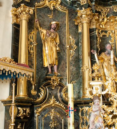 Zdjęcie nr 6: Nastawa ołtarzowa architektoniczna, trójosiowa z bramkami, jednokondygnacyjna ze zwieńczeniem. Ołtarz wysunięty do przodu, drewniany, sarkofagowy, wklęsło-wypukły, zwężający się ku dołowi, na profilowanym cokole, ujęty spływami wolutowymi; dekorowany w narożach palmetami, na froncie rocaille'owy kartusz z malowanymi skrzyżowanymi kluczami w polu. Mensa drewniana z silnie wysuniętą, profilowaną krawędzią, z portatylem z piaskowca. 

Tabernakulum w formie prostopadłościennej skrzynki o wypukłej ściance frontowej, ujęte z przodu ukośnie dostawionymi pilastrami na cokołach z trzonami w formie wolut, dźwigającymi niepełne belkowanie, opasujące je z trzech stron, nad ścianką frontową przyjmujące falistą formę zwieńczoną rocaille'm. Drzwiczki przyjmują kształt stojącego prostokąta zamkniętego łukiem półkolistym nadwieszonym, ujęte profilowaną ramą; w polu płaskorzeźbione przedstawienie kielicha z hostią w glorii na fakturowanym tle. Na belkowaniu, na osi podpór ustawiona jest para rocaille'owych lichtarzy. Tron wystawienia architektoniczny, trójosiowy; oś środkowa ponad tabernakulum w postaci ażurowej niszy z cokołem na pasyjkę, tylna ścianka utworzona z rocaille'u z kłosami zbóż; flankowana pilastrami zwieńczonymi falistym gzymsem, dźwigającymi ażurową, zamkniętą koronę. Podpory przechodzą w spływy wolutowe, ujmujące tabernakulum, na których końcach siedzi para adorujących puttów. Osie boczne są ujęte po bokach pilastrami dźwigającymi imposty podtrzymywane przez rocaille w partii trzonów oraz płonące wazony; pola wypełnione ażurowym rocaille'm i palmetami przechodzącymi w podwójne lichtarze.

Retabulum na planie półowalu, osie boczne ustawione prostopadle do środkowej. Oś środkowa posadowiona na wysokim, dwustrefowym cokole. W pierwszej strefie cokołu prostokątna płycina z napisem: „Z INICJATYWY / KS. PROBOSZCZA ROMANA GORCZYŃSKIEGO / W LATACH 2001 - 2006 / WYKONANO REMONT KOŚCIOŁA I KONSERWACJĘ / WYPOSAŻENIA”. W drugiej strefie cokołu, pośrodku płycina w formie leżącego prostokąta o fantazyjnie wyciętych bokach z malowanym kartuszem herbowym, dzielonym na cztery pola. W lewym górnym polu kartusza umieszczony jest orzeł, poniżej dwójka dzieci w łódce, a po prawej stronie tarczy, w prawym górnym polu dwójka dzieci w łódce, poniżej orzeł. U spodu napis z chronostychem: „EREXIT, AC EXORNAVIT HONORIBVS SANCTI PETRI, / AC PAVLI APOSTOLI ILLVSTRISSIMVS LIBER BAR I WNBS(?) IOANELLY / A TOLVANA PROPPII X I”. Klejnotem jest hełm z pióropuszem zakończony półpostacią rycerza w zbroi, zaś labry mają formę bujnej wici akantowej.  Ryzality cokołów ozdobione są z trzech stron rocaille'owymi płycinami; skrajne konsole rocaille'm i różanymi gałązkami. Oś główna flankowana parą kolumn ustawioną na tle zwielokrotnionych pilastrów. Podpory dźwigają pełne belkowanie, przerwane nad polem środkowym, wyłamane na ich osi oraz przerwany wolutowy przyczółek. W polu środkowym podwójna, profilowana rama w formie stojącego prostokąta zamkniętego łukiem nadwieszonym z uskokami z obrazem św. Piotra i św. Pawła; flankowana przez figury św. Szymona po lewej stronie i św. Judy Tadeusza po prawej, ustawionymi na rocaille'owych wspornikach. Ramy obrazu, trzony wewnętrznych pilastrów i pola za środkową parą figur dekorowane rocaille'm. 

Zwieńczenie w formie zbliżonej do stojącego prostokąta, ujęte spływami wolutowymi, zamknięte falistym gzymsem przechodzącym w antytetycznie zwrócone woluty. Całość zwieńczona gołębicą Ducha Świętego w glorii promienistej. W polu rzeźbiarska grupa Koronacji Marii w glorii promienistej, pośród obłoków i uskrzydlonych główek anielskich. Dwa flankujące grupę putta  na obłokach trzymają banderole z napisem: „FILIA DEI PATRIS” i „MATER DEI FILII”, a kolejne dwa usadzone na szczycie: „VENI CORONABERIS” oraz „VENI SPONSA MEA”. Poniżej zwieńczenia w ażurowym kartuszu znajduje się napis: „QVA E/ST ISTA / QVAE PROGREDI/TUR QVASI AURORA / CONSURGENS / Cant 6.”. Na przyczółku siedzące figury św. Joachima po lewej stronie i św. Józefa po prawej, na gzymsie flankującym pole środkowe dwa putta trzymające słońce i księżyc, na zewnętrznych osiach dwa adorujące anioły. Spływy zwieńczenia dekorowane strzępiastymi liśćmi palmowymi, muszlą i rocaille’m. 

Osie boczne ustawione są na wysokim cokole, od zewnątrz ujęte pilastrami przechodzącymi w woluty, od wewnątrz sąsiadują z osią środkową. Pośrodku bramki z drzwiczkami zakończonymi gzymsem przyjmującym formę cokołu dla figur. Drzwiczki w formie stojącego prostokątna zamkniętego łukiem segmentowym nadwieszonym; osie na skraju ujęte konsolami stanowiącymi cokoły dla podpór. Ryzalit bramek zdobiony płyciną ze strzępiastym grzebieniem; drzwiczki z płyciną z rocaille'm i kwiatowym zwisem na wstążce; powyższy cokół ujęty liśćmi palmowymi i rocaille'm. Kondygnacja flankowana na skraju kolumną ustawioną na tle pilastru, które podtrzymują wyłamany gzyms zakończony wolutami ujmującymi szczyt o falistym przebiegu, na którym ustawiony jest duży płomienisty wazon. W polach ustawione są figury: po lewej się Jakuba Starszego, a po prawej św. Filipa. Na zwieńczeniach usadzone dwie figury aniołów. 

Struktura w całości marmoryzowana w kolorze zielono-brązowym; ornamentyka, kolumny złocone, detale srebrzone. Wszystkie kolumny w jednej trzeciej wysokości przedzielone rocaille’m, a fryz z elementami dekoracji rokokowej. Tabernakulum i tron wystawienia w całości złocone.

