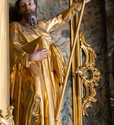 Zdjęcie nr 27: Nastawa ołtarzowa architektoniczna, trójosiowa z bramkami, jednokondygnacyjna ze zwieńczeniem. Ołtarz wysunięty do przodu, drewniany, sarkofagowy, wklęsło-wypukły, zwężający się ku dołowi, na profilowanym cokole, ujęty spływami wolutowymi; dekorowany w narożach palmetami, na froncie rocaille&#039;owy kartusz z malowanymi skrzyżowanymi kluczami w polu. Mensa drewniana z silnie wysuniętą, profilowaną krawędzią, z portatylem z piaskowca. 

Tabernakulum w formie prostopadłościennej skrzynki o wypukłej ściance frontowej, ujęte z przodu ukośnie dostawionymi pilastrami na cokołach z trzonami w formie wolut, dźwigającymi niepełne belkowanie, opasujące je z trzech stron, nad ścianką frontową przyjmujące falistą formę zwieńczoną rocaille&#039;m. Drzwiczki przyjmują kształt stojącego prostokąta zamkniętego łukiem półkolistym nadwieszonym, ujęte profilowaną ramą; w polu płaskorzeźbione przedstawienie kielicha z hostią w glorii na fakturowanym tle. Na belkowaniu, na osi podpór ustawiona jest para rocaille&#039;owych lichtarzy. Tron wystawienia architektoniczny, trójosiowy; oś środkowa ponad tabernakulum w postaci ażurowej niszy z cokołem na pasyjkę, tylna ścianka utworzona z rocaille&#039;u z kłosami zbóż; flankowana pilastrami zwieńczonymi falistym gzymsem, dźwigającymi ażurową, zamkniętą koronę. Podpory przechodzą w spływy wolutowe, ujmujące tabernakulum, na których końcach siedzi para adorujących puttów. Osie boczne są ujęte po bokach pilastrami dźwigającymi imposty podtrzymywane przez rocaille w partii trzonów oraz płonące wazony; pola wypełnione ażurowym rocaille&#039;m i palmetami przechodzącymi w podwójne lichtarze.

Retabulum na planie półowalu, osie boczne ustawione prostopadle do środkowej. Oś środkowa posadowiona na wysokim, dwustrefowym cokole. W pierwszej strefie cokołu prostokątna płycina z napisem: „Z INICJATYWY / KS. PROBOSZCZA ROMANA GORCZYŃSKIEGO / W LATACH 2001 - 2006 / WYKONANO REMONT KOŚCIOŁA I KONSERWACJĘ / WYPOSAŻENIA”. W drugiej strefie cokołu, pośrodku płycina w formie leżącego prostokąta o fantazyjnie wyciętych bokach z malowanym kartuszem herbowym, dzielonym na cztery pola. W lewym górnym polu kartusza umieszczony jest orzeł, poniżej dwójka dzieci w łódce, a po prawej stronie tarczy, w prawym górnym polu dwójka dzieci w łódce, poniżej orzeł. U spodu napis z chronostychem: „EREXIT, AC EXORNAVIT HONORIBVS SANCTI PETRI, / AC PAVLI APOSTOLI ILLVSTRISSIMVS LIBER BAR I WNBS(?) IOANELLY / A TOLVANA PROPPII X I”. Klejnotem jest hełm z pióropuszem zakończony półpostacią rycerza w zbroi, zaś labry mają formę bujnej wici akantowej.  Ryzality cokołów ozdobione są z trzech stron rocaille&#039;owymi płycinami; skrajne konsole rocaille&#039;m i różanymi gałązkami. Oś główna flankowana parą kolumn ustawioną na tle zwielokrotnionych pilastrów. Podpory dźwigają pełne belkowanie, przerwane nad polem środkowym, wyłamane na ich osi oraz przerwany wolutowy przyczółek. W polu środkowym podwójna, profilowana rama w formie stojącego prostokąta zamkniętego łukiem nadwieszonym z uskokami z obrazem św. Piotra i św. Pawła; flankowana przez figury św. Szymona po lewej stronie i św. Judy Tadeusza po prawej, ustawionymi na rocaille&#039;owych wspornikach. Ramy obrazu, trzony wewnętrznych pilastrów i pola za środkową parą figur dekorowane rocaille&#039;m. 

Zwieńczenie w formie zbliżonej do stojącego prostokąta, ujęte spływami wolutowymi, zamknięte falistym gzymsem przechodzącym w antytetycznie zwrócone woluty. Całość zwieńczona gołębicą Ducha Świętego w glorii promienistej. W polu rzeźbiarska grupa Koronacji Marii w glorii promienistej, pośród obłoków i uskrzydlonych główek anielskich. Dwa flankujące grupę putta  na obłokach trzymają banderole z napisem: „FILIA DEI PATRIS” i „MATER DEI FILII”, a kolejne dwa usadzone na szczycie: „VENI CORONABERIS” oraz „VENI SPONSA MEA”. Poniżej zwieńczenia w ażurowym kartuszu znajduje się napis: „QVA E/ST ISTA / QVAE PROGREDI/TUR QVASI AURORA / CONSURGENS / Cant 6.”. Na przyczółku siedzące figury św. Joachima po lewej stronie i św. Józefa po prawej, na gzymsie flankującym pole środkowe dwa putta trzymające słońce i księżyc, na zewnętrznych osiach dwa adorujące anioły. Spływy zwieńczenia dekorowane strzępiastymi liśćmi palmowymi, muszlą i rocaille’m. 

Osie boczne ustawione są na wysokim cokole, od zewnątrz ujęte pilastrami przechodzącymi w woluty, od wewnątrz sąsiadują z osią środkową. Pośrodku bramki z drzwiczkami zakończonymi gzymsem przyjmującym formę cokołu dla figur. Drzwiczki w formie stojącego prostokątna zamkniętego łukiem segmentowym nadwieszonym; osie na skraju ujęte konsolami stanowiącymi cokoły dla podpór. Ryzalit bramek zdobiony płyciną ze strzępiastym grzebieniem; drzwiczki z płyciną z rocaille&#039;m i kwiatowym zwisem na wstążce; powyższy cokół ujęty liśćmi palmowymi i rocaille&#039;m. Kondygnacja flankowana na skraju kolumną ustawioną na tle pilastru, które podtrzymują wyłamany gzyms zakończony wolutami ujmującymi szczyt o falistym przebiegu, na którym ustawiony jest duży płomienisty wazon. W polach ustawione są figury: po lewej się Jakuba Starszego, a po prawej św. Filipa. Na zwieńczeniach usadzone dwie figury aniołów. 

Struktura w całości marmoryzowana w kolorze zielono-brązowym; ornamentyka, kolumny złocone, detale srebrzone. Wszystkie kolumny w jednej trzeciej wysokości przedzielone rocaille’m, a fryz z elementami dekoracji rokokowej. Tabernakulum i tron wystawienia w całości złocone.

