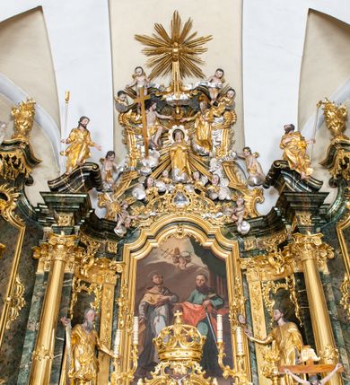 Zdjęcie nr 2: Nastawa ołtarzowa architektoniczna, trójosiowa z bramkami, jednokondygnacyjna ze zwieńczeniem. Ołtarz wysunięty do przodu, drewniany, sarkofagowy, wklęsło-wypukły, zwężający się ku dołowi, na profilowanym cokole, ujęty spływami wolutowymi; dekorowany w narożach palmetami, na froncie rocaille&#039;owy kartusz z malowanymi skrzyżowanymi kluczami w polu. Mensa drewniana z silnie wysuniętą, profilowaną krawędzią, z portatylem z piaskowca. 

Tabernakulum w formie prostopadłościennej skrzynki o wypukłej ściance frontowej, ujęte z przodu ukośnie dostawionymi pilastrami na cokołach z trzonami w formie wolut, dźwigającymi niepełne belkowanie, opasujące je z trzech stron, nad ścianką frontową przyjmujące falistą formę zwieńczoną rocaille&#039;m. Drzwiczki przyjmują kształt stojącego prostokąta zamkniętego łukiem półkolistym nadwieszonym, ujęte profilowaną ramą; w polu płaskorzeźbione przedstawienie kielicha z hostią w glorii na fakturowanym tle. Na belkowaniu, na osi podpór ustawiona jest para rocaille&#039;owych lichtarzy. Tron wystawienia architektoniczny, trójosiowy; oś środkowa ponad tabernakulum w postaci ażurowej niszy z cokołem na pasyjkę, tylna ścianka utworzona z rocaille&#039;u z kłosami zbóż; flankowana pilastrami zwieńczonymi falistym gzymsem, dźwigającymi ażurową, zamkniętą koronę. Podpory przechodzą w spływy wolutowe, ujmujące tabernakulum, na których końcach siedzi para adorujących puttów. Osie boczne są ujęte po bokach pilastrami dźwigającymi imposty podtrzymywane przez rocaille w partii trzonów oraz płonące wazony; pola wypełnione ażurowym rocaille&#039;m i palmetami przechodzącymi w podwójne lichtarze.

Retabulum na planie półowalu, osie boczne ustawione prostopadle do środkowej. Oś środkowa posadowiona na wysokim, dwustrefowym cokole. W pierwszej strefie cokołu prostokątna płycina z napisem: „Z INICJATYWY / KS. PROBOSZCZA ROMANA GORCZYŃSKIEGO / W LATACH 2001 - 2006 / WYKONANO REMONT KOŚCIOŁA I KONSERWACJĘ / WYPOSAŻENIA”. W drugiej strefie cokołu, pośrodku płycina w formie leżącego prostokąta o fantazyjnie wyciętych bokach z malowanym kartuszem herbowym, dzielonym na cztery pola. W lewym górnym polu kartusza umieszczony jest orzeł, poniżej dwójka dzieci w łódce, a po prawej stronie tarczy, w prawym górnym polu dwójka dzieci w łódce, poniżej orzeł. U spodu napis z chronostychem: „EREXIT, AC EXORNAVIT HONORIBVS SANCTI PETRI, / AC PAVLI APOSTOLI ILLVSTRISSIMVS LIBER BAR I WNBS(?) IOANELLY / A TOLVANA PROPPII X I”. Klejnotem jest hełm z pióropuszem zakończony półpostacią rycerza w zbroi, zaś labry mają formę bujnej wici akantowej.  Ryzality cokołów ozdobione są z trzech stron rocaille&#039;owymi płycinami; skrajne konsole rocaille&#039;m i różanymi gałązkami. Oś główna flankowana parą kolumn ustawioną na tle zwielokrotnionych pilastrów. Podpory dźwigają pełne belkowanie, przerwane nad polem środkowym, wyłamane na ich osi oraz przerwany wolutowy przyczółek. W polu środkowym podwójna, profilowana rama w formie stojącego prostokąta zamkniętego łukiem nadwieszonym z uskokami z obrazem św. Piotra i św. Pawła; flankowana przez figury św. Szymona po lewej stronie i św. Judy Tadeusza po prawej, ustawionymi na rocaille&#039;owych wspornikach. Ramy obrazu, trzony wewnętrznych pilastrów i pola za środkową parą figur dekorowane rocaille&#039;m. 

Zwieńczenie w formie zbliżonej do stojącego prostokąta, ujęte spływami wolutowymi, zamknięte falistym gzymsem przechodzącym w antytetycznie zwrócone woluty. Całość zwieńczona gołębicą Ducha Świętego w glorii promienistej. W polu rzeźbiarska grupa Koronacji Marii w glorii promienistej, pośród obłoków i uskrzydlonych główek anielskich. Dwa flankujące grupę putta  na obłokach trzymają banderole z napisem: „FILIA DEI PATRIS” i „MATER DEI FILII”, a kolejne dwa usadzone na szczycie: „VENI CORONABERIS” oraz „VENI SPONSA MEA”. Poniżej zwieńczenia w ażurowym kartuszu znajduje się napis: „QVA E/ST ISTA / QVAE PROGREDI/TUR QVASI AURORA / CONSURGENS / Cant 6.”. Na przyczółku siedzące figury św. Joachima po lewej stronie i św. Józefa po prawej, na gzymsie flankującym pole środkowe dwa putta trzymające słońce i księżyc, na zewnętrznych osiach dwa adorujące anioły. Spływy zwieńczenia dekorowane strzępiastymi liśćmi palmowymi, muszlą i rocaille’m. 

Osie boczne ustawione są na wysokim cokole, od zewnątrz ujęte pilastrami przechodzącymi w woluty, od wewnątrz sąsiadują z osią środkową. Pośrodku bramki z drzwiczkami zakończonymi gzymsem przyjmującym formę cokołu dla figur. Drzwiczki w formie stojącego prostokątna zamkniętego łukiem segmentowym nadwieszonym; osie na skraju ujęte konsolami stanowiącymi cokoły dla podpór. Ryzalit bramek zdobiony płyciną ze strzępiastym grzebieniem; drzwiczki z płyciną z rocaille&#039;m i kwiatowym zwisem na wstążce; powyższy cokół ujęty liśćmi palmowymi i rocaille&#039;m. Kondygnacja flankowana na skraju kolumną ustawioną na tle pilastru, które podtrzymują wyłamany gzyms zakończony wolutami ujmującymi szczyt o falistym przebiegu, na którym ustawiony jest duży płomienisty wazon. W polach ustawione są figury: po lewej się Jakuba Starszego, a po prawej św. Filipa. Na zwieńczeniach usadzone dwie figury aniołów. 

Struktura w całości marmoryzowana w kolorze zielono-brązowym; ornamentyka, kolumny złocone, detale srebrzone. Wszystkie kolumny w jednej trzeciej wysokości przedzielone rocaille’m, a fryz z elementami dekoracji rokokowej. Tabernakulum i tron wystawienia w całości złocone.

