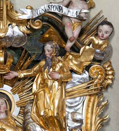 Zdjęcie nr 13: Nastawa ołtarzowa architektoniczna, trójosiowa z bramkami, jednokondygnacyjna ze zwieńczeniem. Ołtarz wysunięty do przodu, drewniany, sarkofagowy, wklęsło-wypukły, zwężający się ku dołowi, na profilowanym cokole, ujęty spływami wolutowymi; dekorowany w narożach palmetami, na froncie rocaille'owy kartusz z malowanymi skrzyżowanymi kluczami w polu. Mensa drewniana z silnie wysuniętą, profilowaną krawędzią, z portatylem z piaskowca. 

Tabernakulum w formie prostopadłościennej skrzynki o wypukłej ściance frontowej, ujęte z przodu ukośnie dostawionymi pilastrami na cokołach z trzonami w formie wolut, dźwigającymi niepełne belkowanie, opasujące je z trzech stron, nad ścianką frontową przyjmujące falistą formę zwieńczoną rocaille'm. Drzwiczki przyjmują kształt stojącego prostokąta zamkniętego łukiem półkolistym nadwieszonym, ujęte profilowaną ramą; w polu płaskorzeźbione przedstawienie kielicha z hostią w glorii na fakturowanym tle. Na belkowaniu, na osi podpór ustawiona jest para rocaille'owych lichtarzy. Tron wystawienia architektoniczny, trójosiowy; oś środkowa ponad tabernakulum w postaci ażurowej niszy z cokołem na pasyjkę, tylna ścianka utworzona z rocaille'u z kłosami zbóż; flankowana pilastrami zwieńczonymi falistym gzymsem, dźwigającymi ażurową, zamkniętą koronę. Podpory przechodzą w spływy wolutowe, ujmujące tabernakulum, na których końcach siedzi para adorujących puttów. Osie boczne są ujęte po bokach pilastrami dźwigającymi imposty podtrzymywane przez rocaille w partii trzonów oraz płonące wazony; pola wypełnione ażurowym rocaille'm i palmetami przechodzącymi w podwójne lichtarze.

Retabulum na planie półowalu, osie boczne ustawione prostopadle do środkowej. Oś środkowa posadowiona na wysokim, dwustrefowym cokole. W pierwszej strefie cokołu prostokątna płycina z napisem: „Z INICJATYWY / KS. PROBOSZCZA ROMANA GORCZYŃSKIEGO / W LATACH 2001 - 2006 / WYKONANO REMONT KOŚCIOŁA I KONSERWACJĘ / WYPOSAŻENIA”. W drugiej strefie cokołu, pośrodku płycina w formie leżącego prostokąta o fantazyjnie wyciętych bokach z malowanym kartuszem herbowym, dzielonym na cztery pola. W lewym górnym polu kartusza umieszczony jest orzeł, poniżej dwójka dzieci w łódce, a po prawej stronie tarczy, w prawym górnym polu dwójka dzieci w łódce, poniżej orzeł. U spodu napis z chronostychem: „EREXIT, AC EXORNAVIT HONORIBVS SANCTI PETRI, / AC PAVLI APOSTOLI ILLVSTRISSIMVS LIBER BAR I WNBS(?) IOANELLY / A TOLVANA PROPPII X I”. Klejnotem jest hełm z pióropuszem zakończony półpostacią rycerza w zbroi, zaś labry mają formę bujnej wici akantowej.  Ryzality cokołów ozdobione są z trzech stron rocaille'owymi płycinami; skrajne konsole rocaille'm i różanymi gałązkami. Oś główna flankowana parą kolumn ustawioną na tle zwielokrotnionych pilastrów. Podpory dźwigają pełne belkowanie, przerwane nad polem środkowym, wyłamane na ich osi oraz przerwany wolutowy przyczółek. W polu środkowym podwójna, profilowana rama w formie stojącego prostokąta zamkniętego łukiem nadwieszonym z uskokami z obrazem św. Piotra i św. Pawła; flankowana przez figury św. Szymona po lewej stronie i św. Judy Tadeusza po prawej, ustawionymi na rocaille'owych wspornikach. Ramy obrazu, trzony wewnętrznych pilastrów i pola za środkową parą figur dekorowane rocaille'm. 

Zwieńczenie w formie zbliżonej do stojącego prostokąta, ujęte spływami wolutowymi, zamknięte falistym gzymsem przechodzącym w antytetycznie zwrócone woluty. Całość zwieńczona gołębicą Ducha Świętego w glorii promienistej. W polu rzeźbiarska grupa Koronacji Marii w glorii promienistej, pośród obłoków i uskrzydlonych główek anielskich. Dwa flankujące grupę putta  na obłokach trzymają banderole z napisem: „FILIA DEI PATRIS” i „MATER DEI FILII”, a kolejne dwa usadzone na szczycie: „VENI CORONABERIS” oraz „VENI SPONSA MEA”. Poniżej zwieńczenia w ażurowym kartuszu znajduje się napis: „QVA E/ST ISTA / QVAE PROGREDI/TUR QVASI AURORA / CONSURGENS / Cant 6.”. Na przyczółku siedzące figury św. Joachima po lewej stronie i św. Józefa po prawej, na gzymsie flankującym pole środkowe dwa putta trzymające słońce i księżyc, na zewnętrznych osiach dwa adorujące anioły. Spływy zwieńczenia dekorowane strzępiastymi liśćmi palmowymi, muszlą i rocaille’m. 

Osie boczne ustawione są na wysokim cokole, od zewnątrz ujęte pilastrami przechodzącymi w woluty, od wewnątrz sąsiadują z osią środkową. Pośrodku bramki z drzwiczkami zakończonymi gzymsem przyjmującym formę cokołu dla figur. Drzwiczki w formie stojącego prostokątna zamkniętego łukiem segmentowym nadwieszonym; osie na skraju ujęte konsolami stanowiącymi cokoły dla podpór. Ryzalit bramek zdobiony płyciną ze strzępiastym grzebieniem; drzwiczki z płyciną z rocaille'm i kwiatowym zwisem na wstążce; powyższy cokół ujęty liśćmi palmowymi i rocaille'm. Kondygnacja flankowana na skraju kolumną ustawioną na tle pilastru, które podtrzymują wyłamany gzyms zakończony wolutami ujmującymi szczyt o falistym przebiegu, na którym ustawiony jest duży płomienisty wazon. W polach ustawione są figury: po lewej się Jakuba Starszego, a po prawej św. Filipa. Na zwieńczeniach usadzone dwie figury aniołów. 

Struktura w całości marmoryzowana w kolorze zielono-brązowym; ornamentyka, kolumny złocone, detale srebrzone. Wszystkie kolumny w jednej trzeciej wysokości przedzielone rocaille’m, a fryz z elementami dekoracji rokokowej. Tabernakulum i tron wystawienia w całości złocone.

