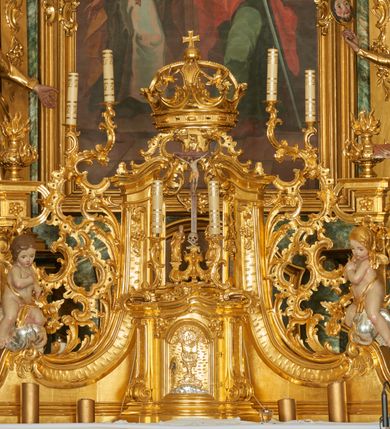 Zdjęcie nr 1: Tabernakulum w formie prostopadłościennej skrzynki o wypukłej ściance frontowej, ujęte z przodu ukośnie dostawionymi pilastrami na cokołach z trzonami w formie wolut, dźwigającymi niepełne belkowanie, opasujące je z trzech stron, nad ścianką frontową przyjmujące falistą formę zwieńczoną rocaille'm. Drzwiczki przyjmują kształt stojącego prostokąta zamkniętego łukiem półkolistym nadwieszonym, ujęte profilowaną ramą; w polu płaskorzeźbione przedstawienie kielicha z hostią w glorii na fakturowanym tle. Na belkowaniu, na osi podpór ustawiona jest para rocaille'owych lichtarzy. 
Tron wystawienia architektoniczny, trójosiowy; oś środkowa ponad tabernakulum w postaci ażurowej niszy z cokołem na pasyjkę, tylna ścianka utworzona z rocaille'u z kłosami zbóż; flankowana pilastrami zwieńczonymi falistym gzymsem, dźwigającymi ażurową, zamkniętą koronę. Podpory przechodzą w spływy wolutowe, ujmujące tabernakulum, na których końcach siedzi para adorujących puttów. Osie boczne ujęte po bokach pilastrami dźwigającymi imposty podtrzymywane przez rocaille w partii trzonów oraz płonące wazony; pola wypełnione ażurowym rocaille'm i palmetami przechodzącymi w podwójne lichtarze.
