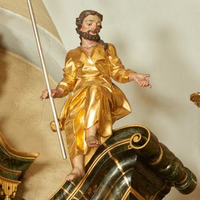 Zdjęcie nr 1: Rzeźba św. Joachima ścięta z tyłu, drążona, ustawiona na przyczółku ołtarza. Święty zwrócony trzy czwarte w prawo, ukazany w pozycji siedzącej z lewą nogą ugiętą w kolanie i delikatnie uniesioną do góry, ręce szeroko rozłożone na boki, w prawej trzyma kij pasterski o zakończeniu w kształcie szufli. Twarz szeroka o wyraźnie zaznaczonych kościach policzkowych, dużych oczach i nosie, policzki i nos silnie zarumienione, twarz okolona krótką brodą. Włosy długie, ciemnobrązowe spływające na plecy i lewe ramię. Święty ubrany jest w długą suknię z długimi i wąskimi rękawami, zawiniętymi na mankietach, drapowaną w grube i ostro łamane fałdy z dekoltem w kształcie litery „V”. Polichromia naturalistyczna w odsłoniętych partiach ciała; szaty złocone, szufla złocona o srebrzonym drzewcu.