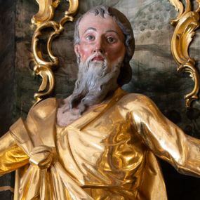 Zdjęcie nr 1: Rzeźba św. Szymona ścięta z tyłu, drążona, ustawiona na kostce. Święty ukazany frontalnie w delikatnym kontrapoście z lewą nogą ugiętą w kolanie. Ręce ma rozłożone szeroko na boki, w lewej trzyma piłę. Twarz szeroka o wyraźnie zaznaczonych kościach policzkowych, dużych oczach i małych ustach, policzki silnie zarumienione, twarz okolona długą i siwą brodą. Włosy długie, siwe, spływające na plecy i małymi kosmykami na czoło. Święty ubrany jest w długą suknię z długimi i wąskimi rękawami, zawiniętymi na mankietach, drapowaną w grube i miękkie fałdy. Na prawe ramię narzucony ma długi płaszcz, przewiązany diagonalnie na torsie wstążką. Polichromia naturalistyczna w odsłoniętych partiach ciała; szaty i atrybuty złocone, piła srebrzona.

