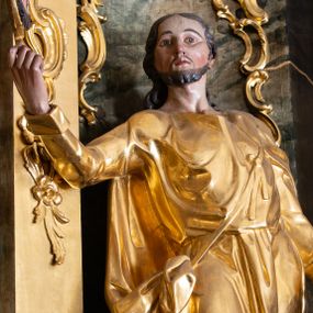 Zdjęcie nr 1: Rzeźba św. Judy Tadeusza ścięta z tyłu, drążona, ustawiona na kostce. Święty ukazany frontalnie w silnym kontrapoście z prawą nogą ugiętą w kolanie. W prawej, uniesionej do góry ręce trzyma medalion z wizerunkiem Chrystusa, a w lewej opuszczonej wzdłuż ciała podtrzymuje pałkę. Twarz szeroka o wyraźnie zaznaczonych kościach policzkowych, dużych oczach i delikatnie rozchylonych ustach, policzki silnie zarumienione, twarz okolona krótką brodą. Włosy długie, ciemnobrązowe spływające na plecy. Święty ubrany jest w suknię sięgającą za kolana z długimi i wąskimi rękawami, zawiniętymi na mankietach, drapowaną w grube i miękkie fałdy. Na lewe ramię narzucony długi płaszcz, przewiązany diagonalnie na torsie wstążką. Polichromia naturalistyczna w odsłoniętych partiach ciała; szaty i atrybuty złocone, pałka srebrzona.
