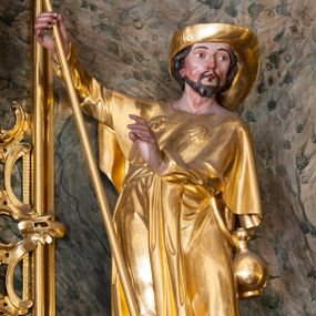 Zdjęcie nr 1: Rzeźba św. Jakuba Starszego ścięta z tyłu, drążona, ustawiona na prostopadłościennej kostce. Święty ukazany frontalnie w silnym kontrapoście z lewą nogą ugiętą w kolanie. W prawej, uniesionej do góry ręce trzyma laskę pielgrzyma. Lewą rękę, ugiętą w łokciu wyciąga przed siebie. Twarz szeroka o wyraźnie zaznaczonych kościach policzkowych, dużych oczach i delikatnie rozchylonych ustach, policzki silnie zarumienione, twarz okolona krótką brodą. Włosy krótkie, ciemnobrązowe schowane pod kapeluszem. Święty ubrany jest w suknię sięgającą połowy łydek z długimi i wąskimi rękawami, zawiniętymi na mankietach, drapowaną w grube i miękkie fałdy. Na ramiona ma narzuconą krótką pelerynę z dwiema muszlami na piersi, a przy boku zawieszony bukłak. Polichromia naturalistyczna w odsłoniętych partiach ciała; szaty i atrybuty złocone.