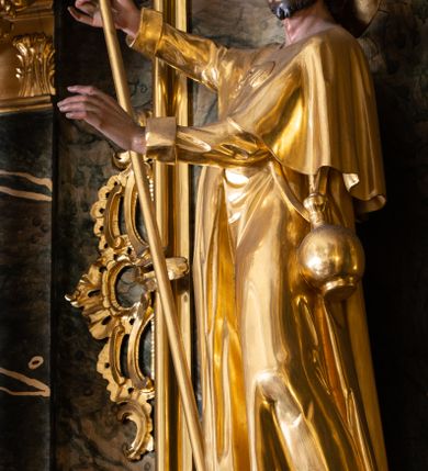 Zdjęcie nr 2: Rzeźba św. Jakuba Starszego ścięta z tyłu, drążona, ustawiona na prostopadłościennej kostce. Święty ukazany frontalnie w silnym kontrapoście z lewą nogą ugiętą w kolanie. W prawej, uniesionej do góry ręce trzyma laskę pielgrzyma. Lewą rękę, ugiętą w łokciu wyciąga przed siebie. Twarz szeroka o wyraźnie zaznaczonych kościach policzkowych, dużych oczach i delikatnie rozchylonych ustach, policzki silnie zarumienione, twarz okolona krótką brodą. Włosy krótkie, ciemnobrązowe schowane pod kapeluszem. Święty ubrany jest w suknię sięgającą połowy łydek z długimi i wąskimi rękawami, zawiniętymi na mankietach, drapowaną w grube i miękkie fałdy. Na ramiona ma narzuconą krótką pelerynę z dwiema muszlami na piersi, a przy boku zawieszony bukłak. Polichromia naturalistyczna w odsłoniętych partiach ciała; szaty i atrybuty złocone.